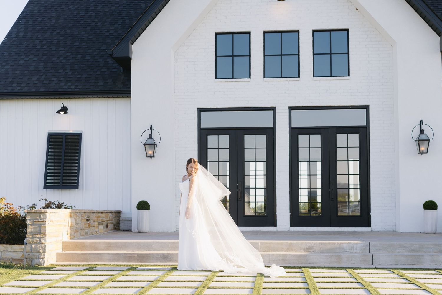 Modern white farmhouse exterior with black windows serves as backdrop for bridal photography.
