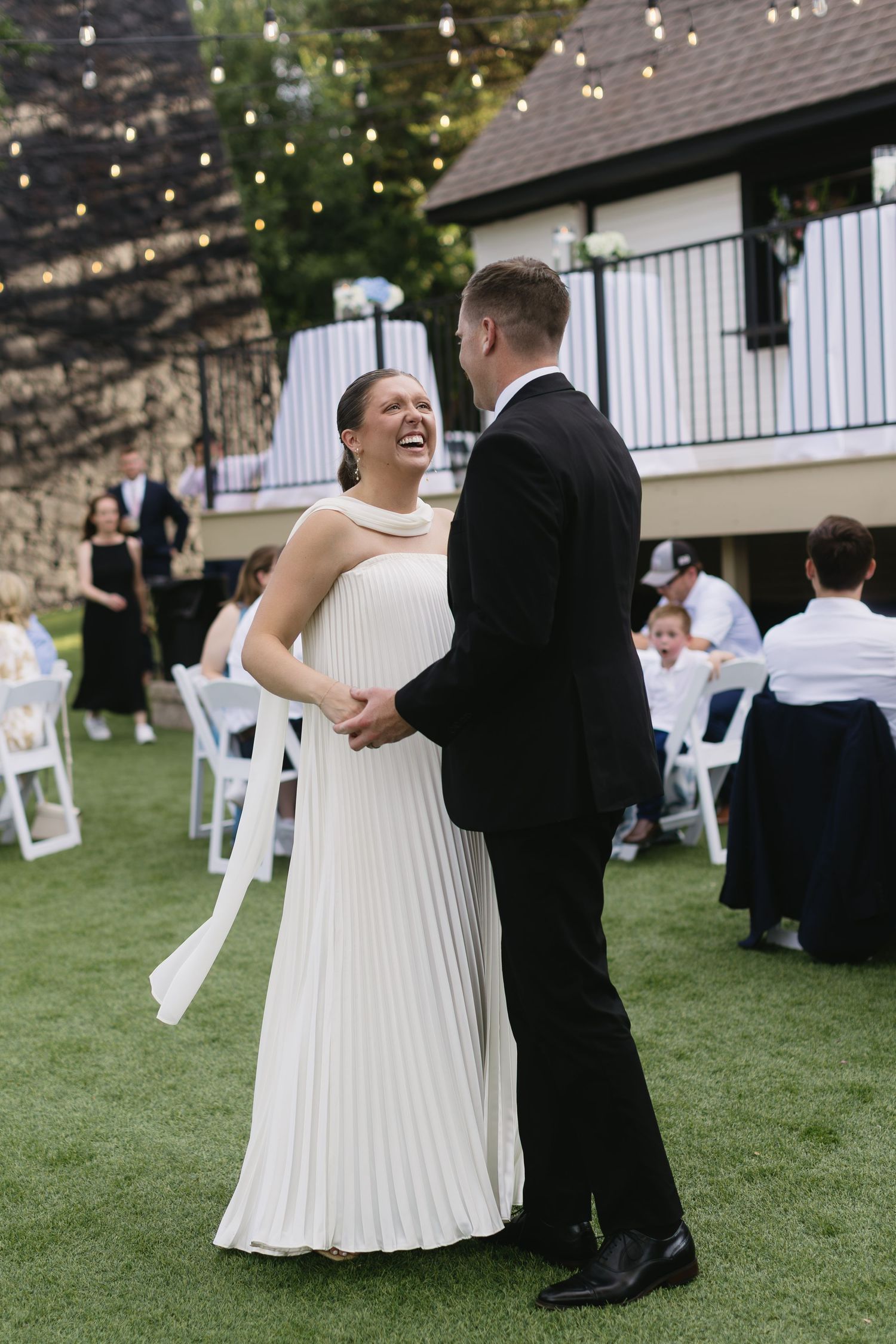 Wedding reception on lawn with string lights and white chairs under evening sky.