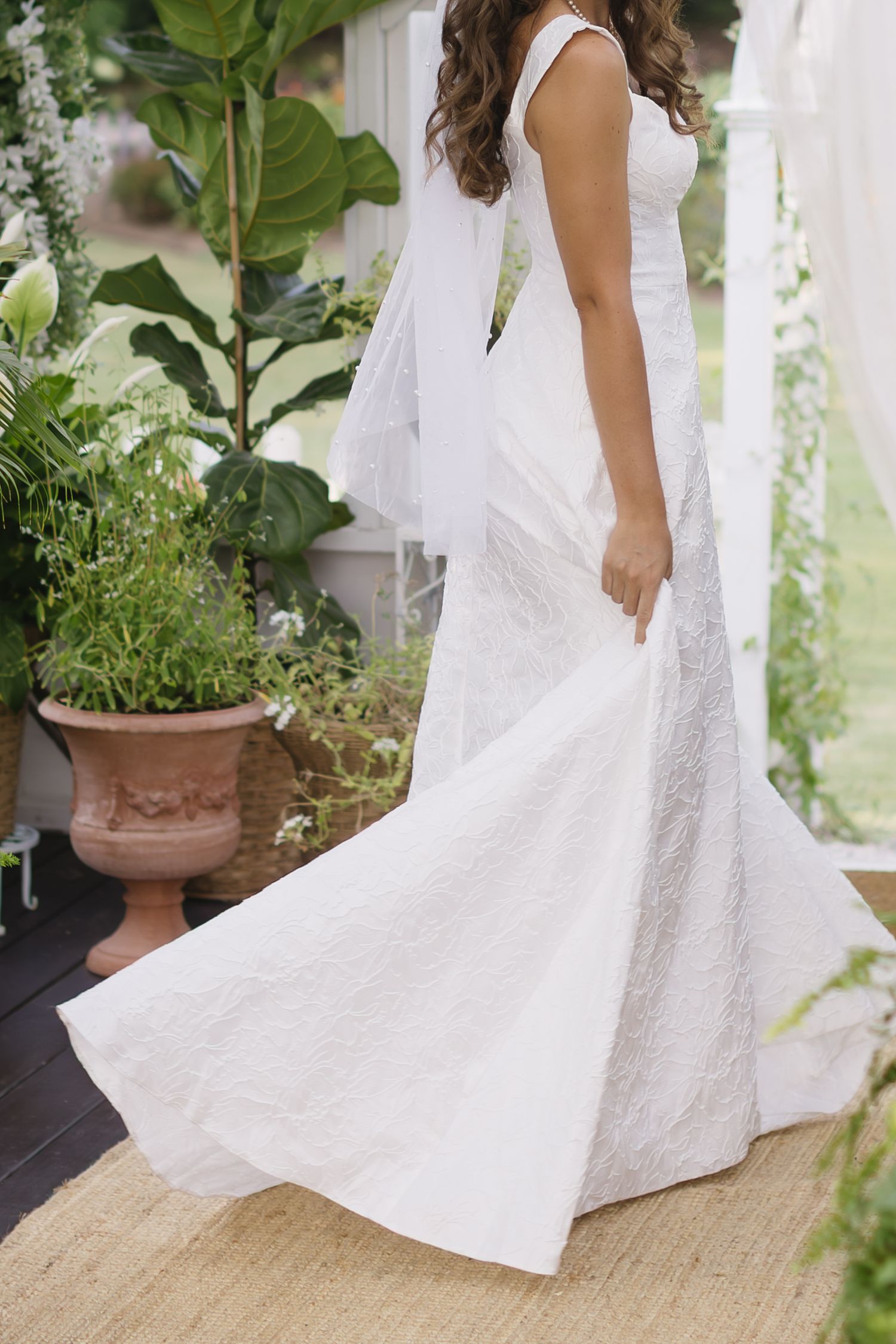 Close-up details of a flowing white lace wedding dress with delicate patterns shown from multiple angles in a garden setting.