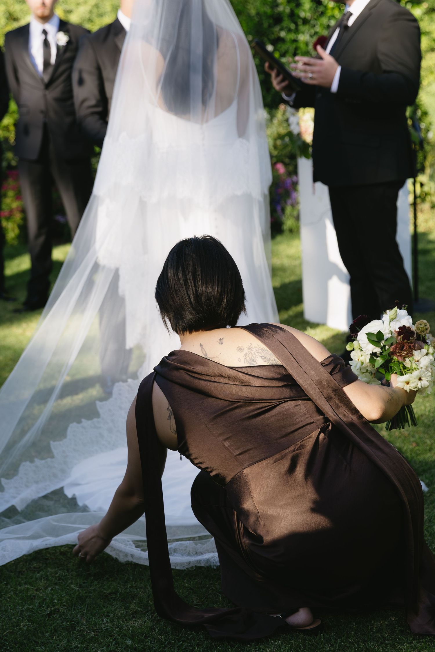 A bridesmaid in a brown dress playfully poses on the grass during wedding photos.