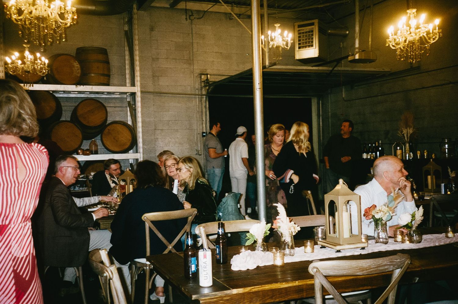 Wedding reception dinner in industrial venue with chandeliers and wine barrels.