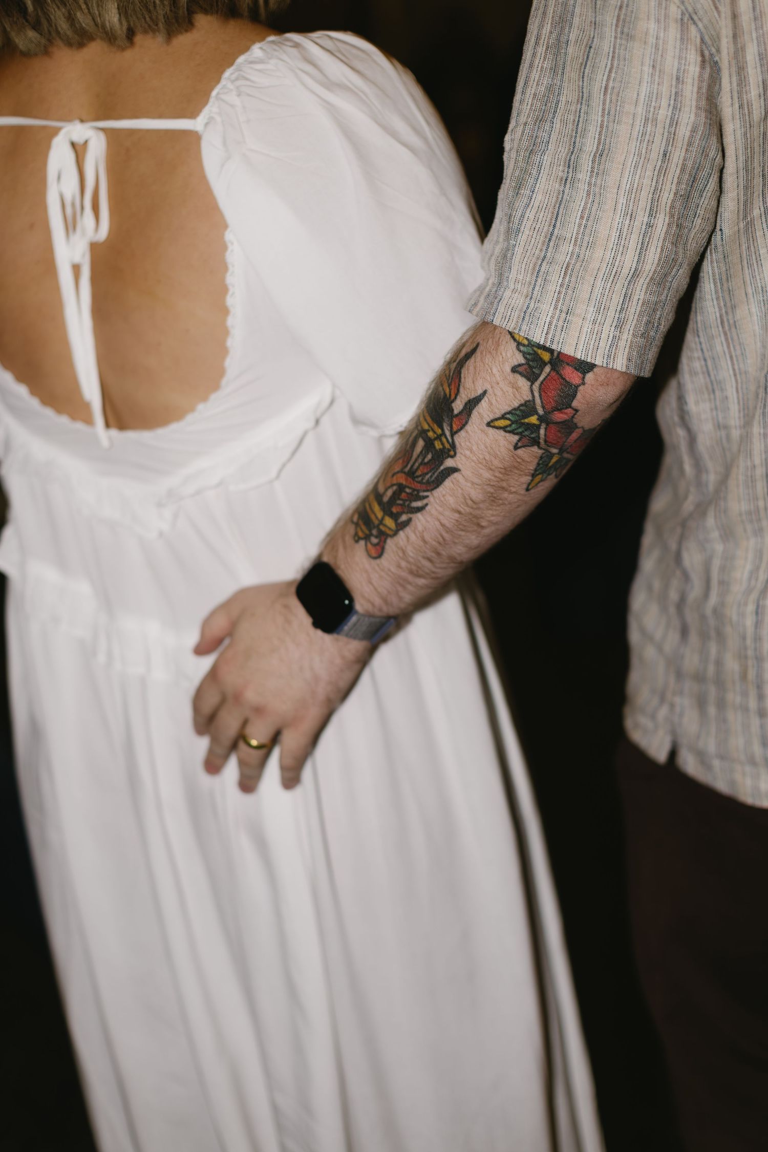 Close-up view of tattooed arms against a white dress showing intricate body art details.