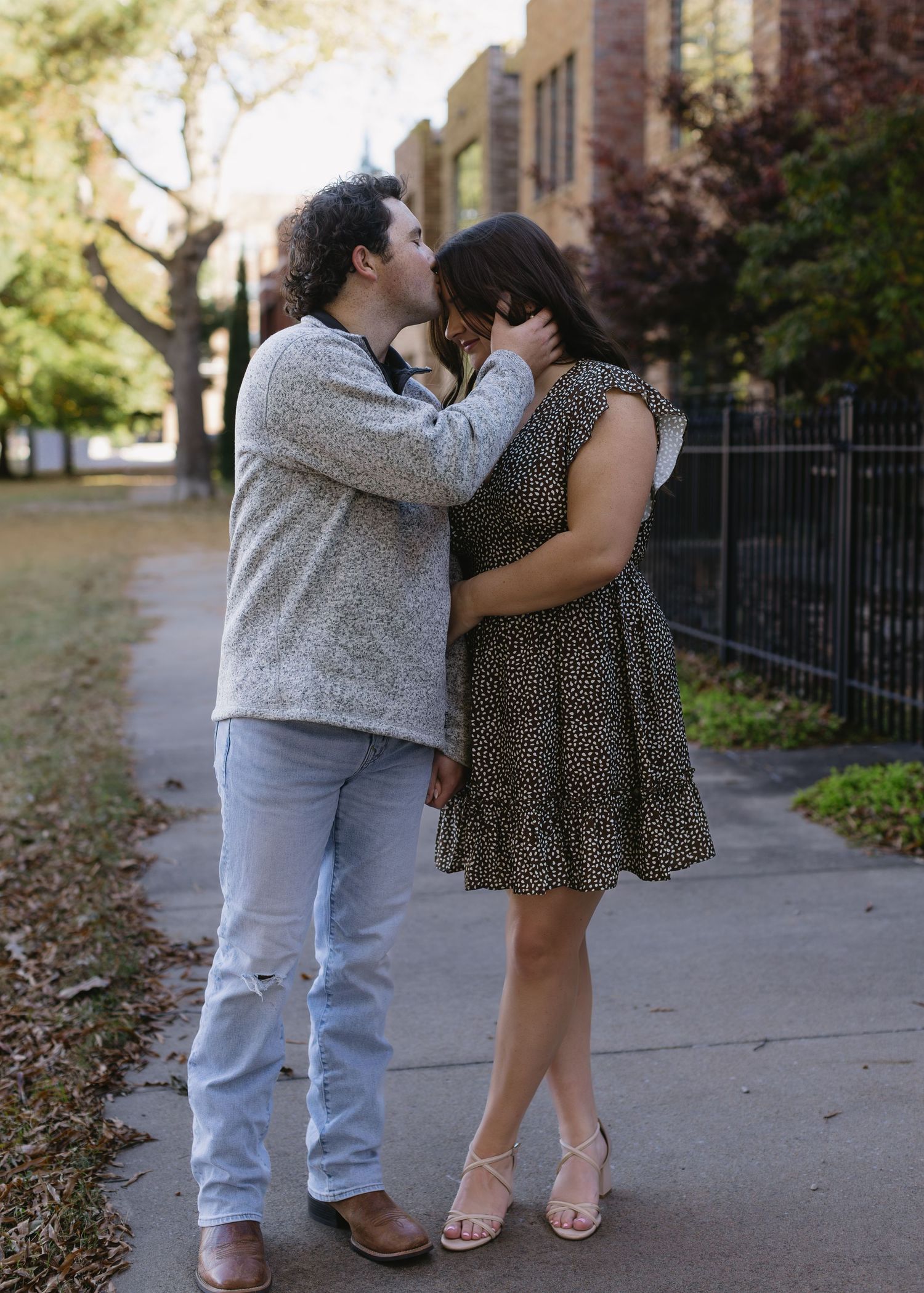 A couple shares a tender moment on a path near autumn trees.