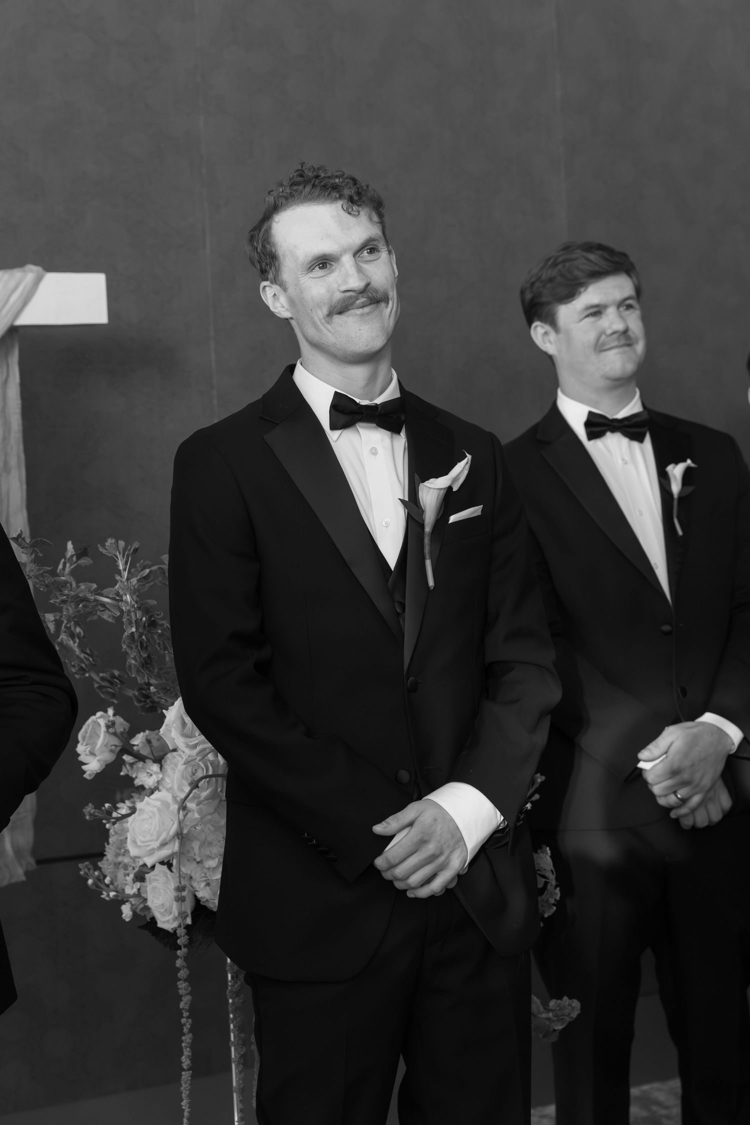 Groomsmen in classic black tuxedos and bowties lined up against grey backdrop.