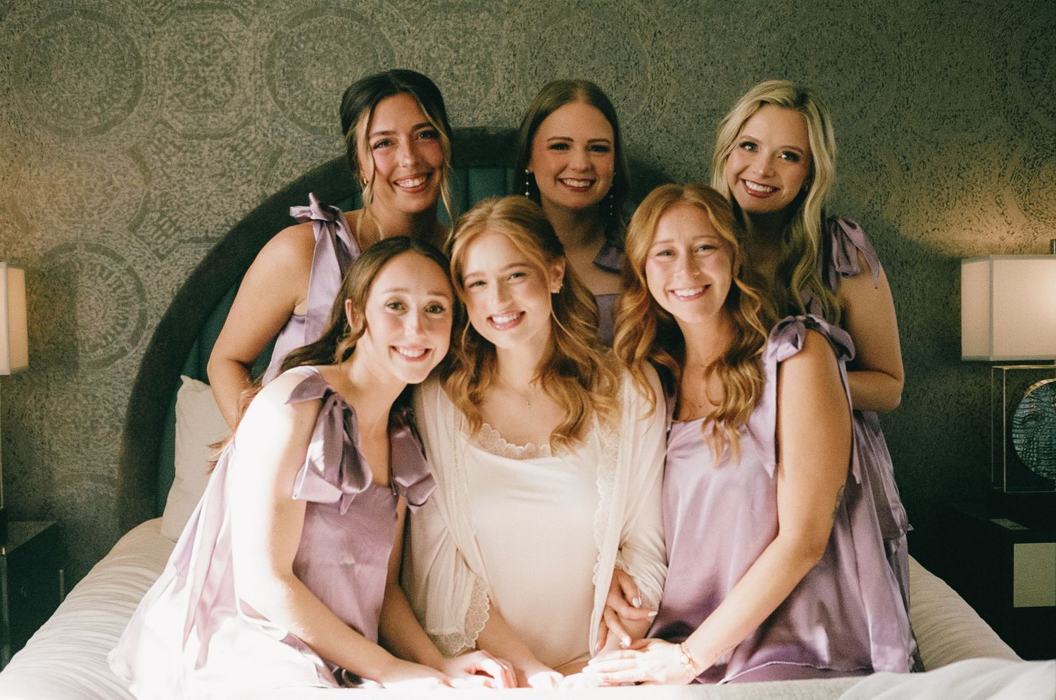 Bridal party in soft pink dresses posing together on couch.