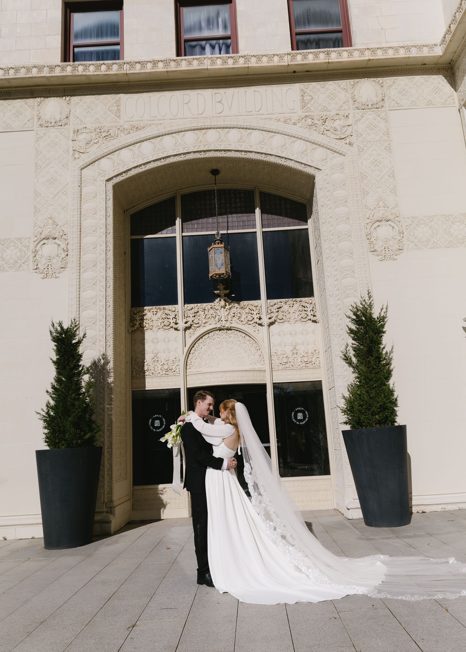 A wedding photo series showing a couple posing against an elegant white stone building with ornate architectural details.