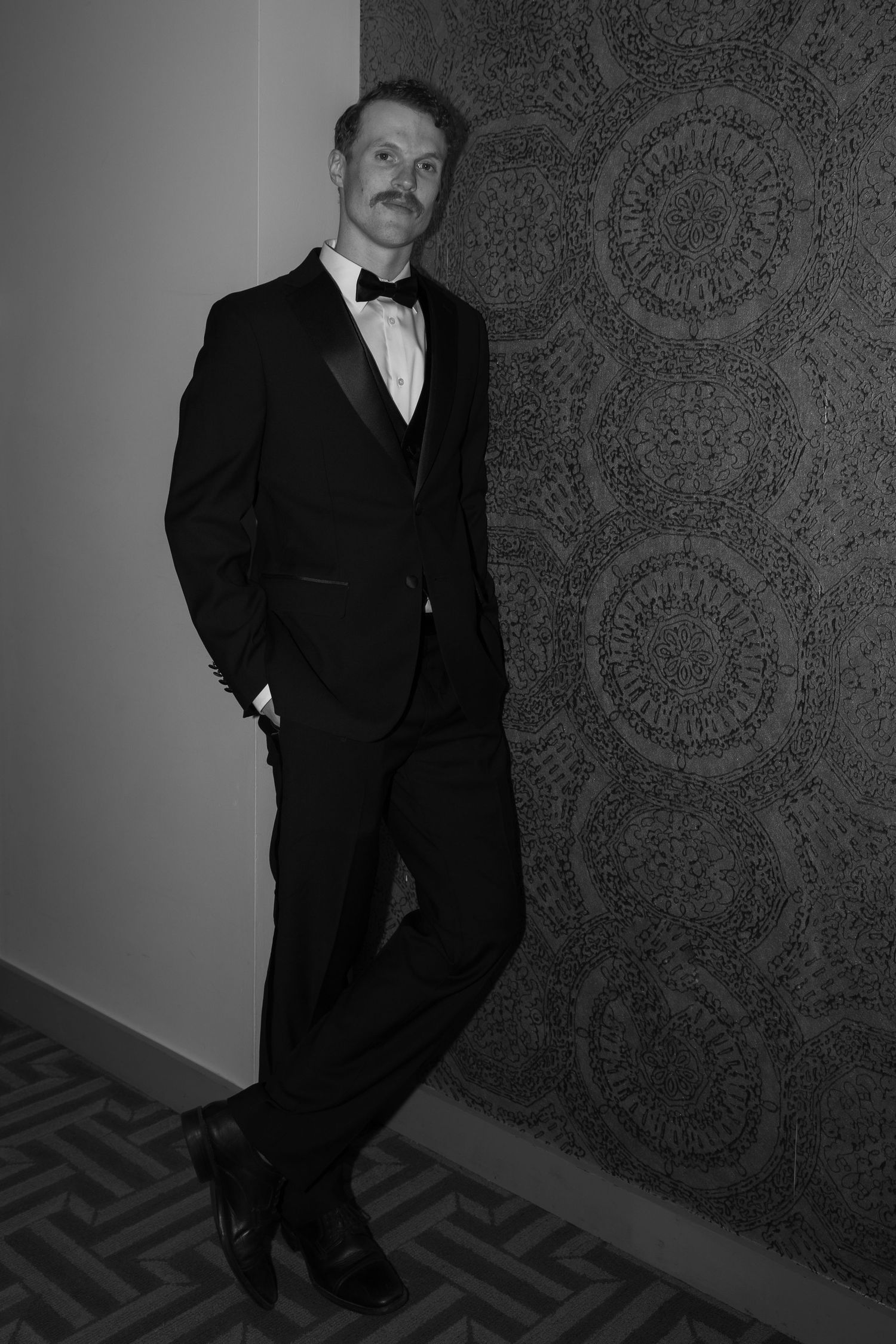 Classic black tuxedo photographed against textured wallpaper in dramatic lighting.