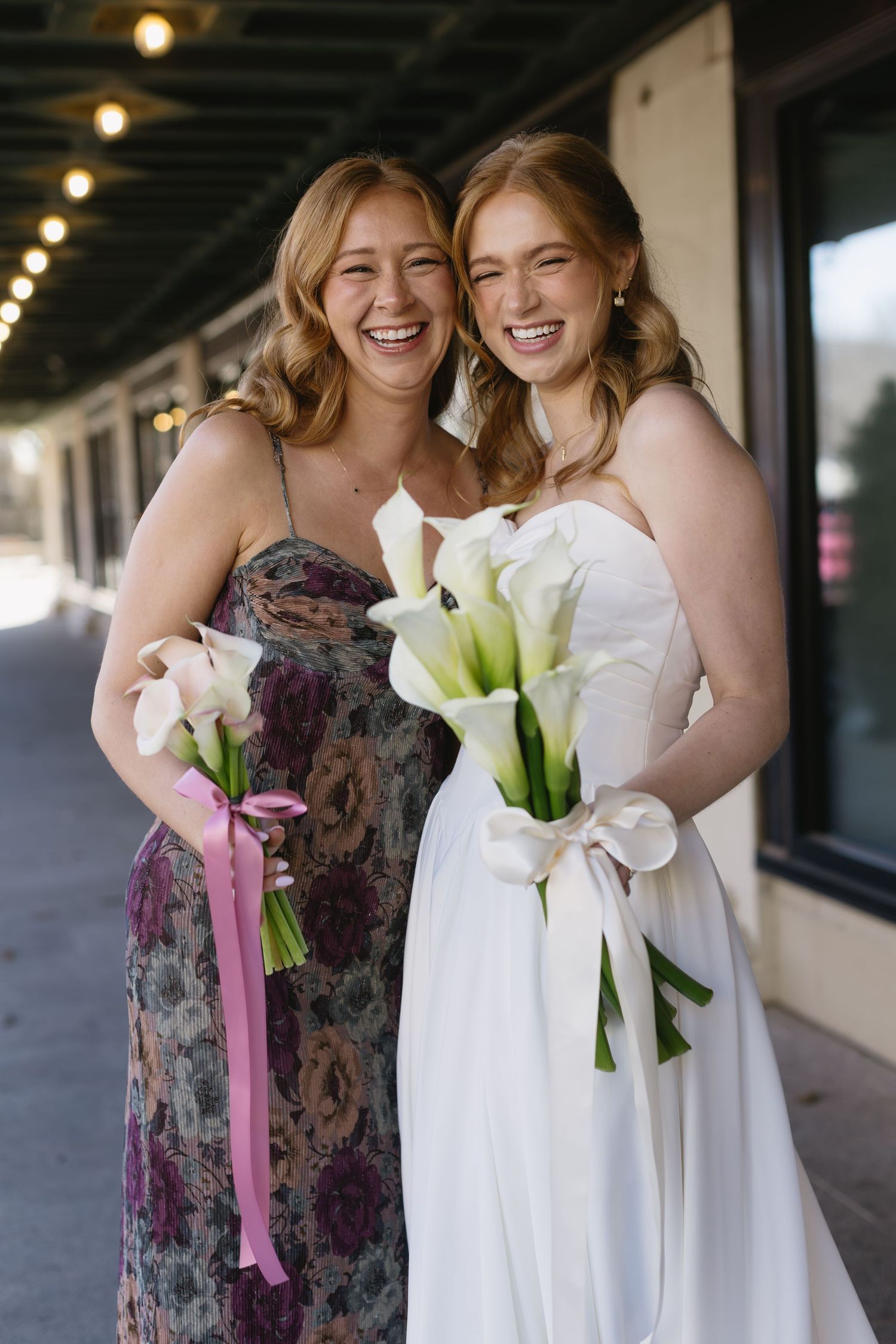 Wedding party with mix of floral print and white dresses holding elegant calla lily bouquets.