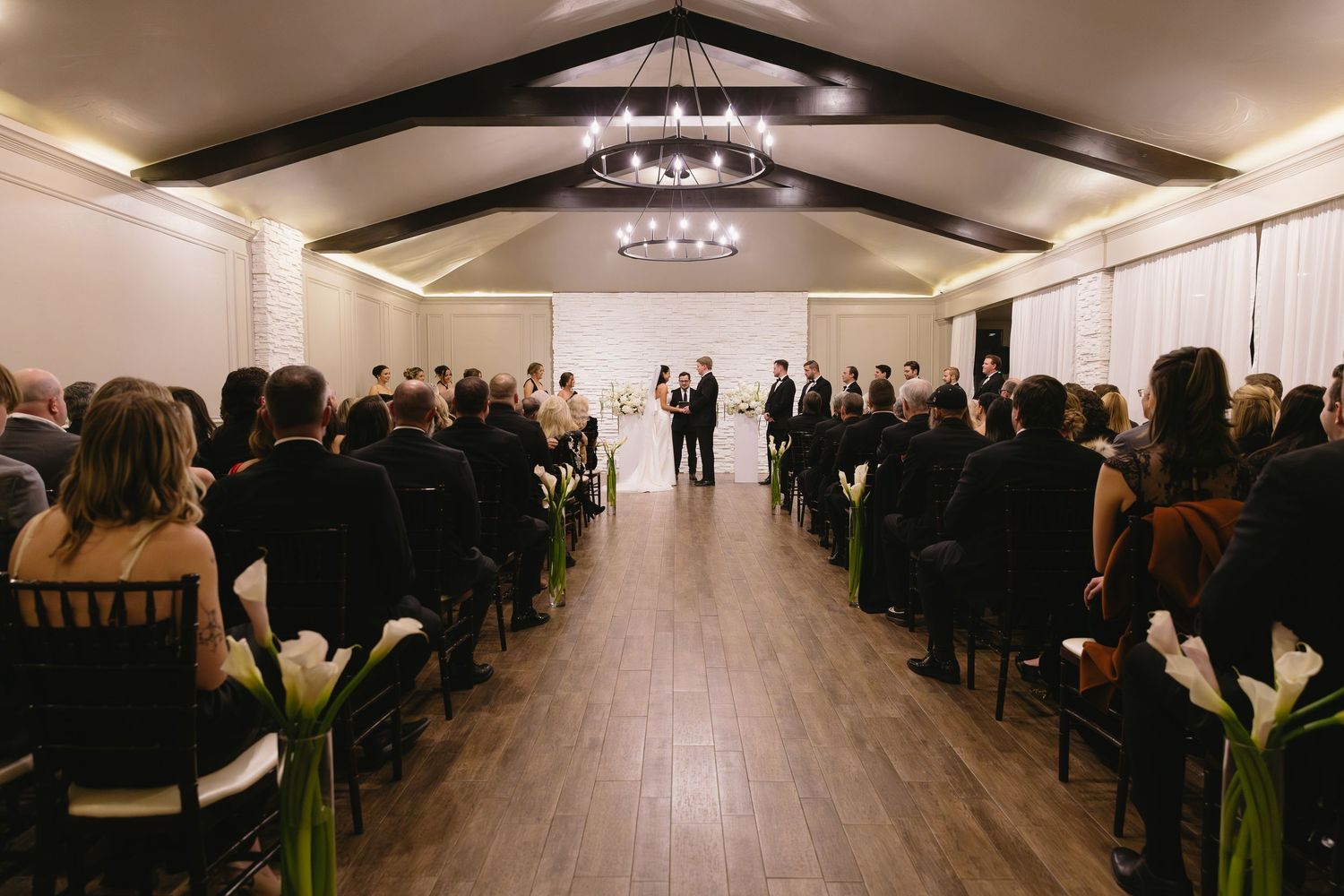 Wide view of wedding ceremony venue with white draping and vaulted ceiling.
