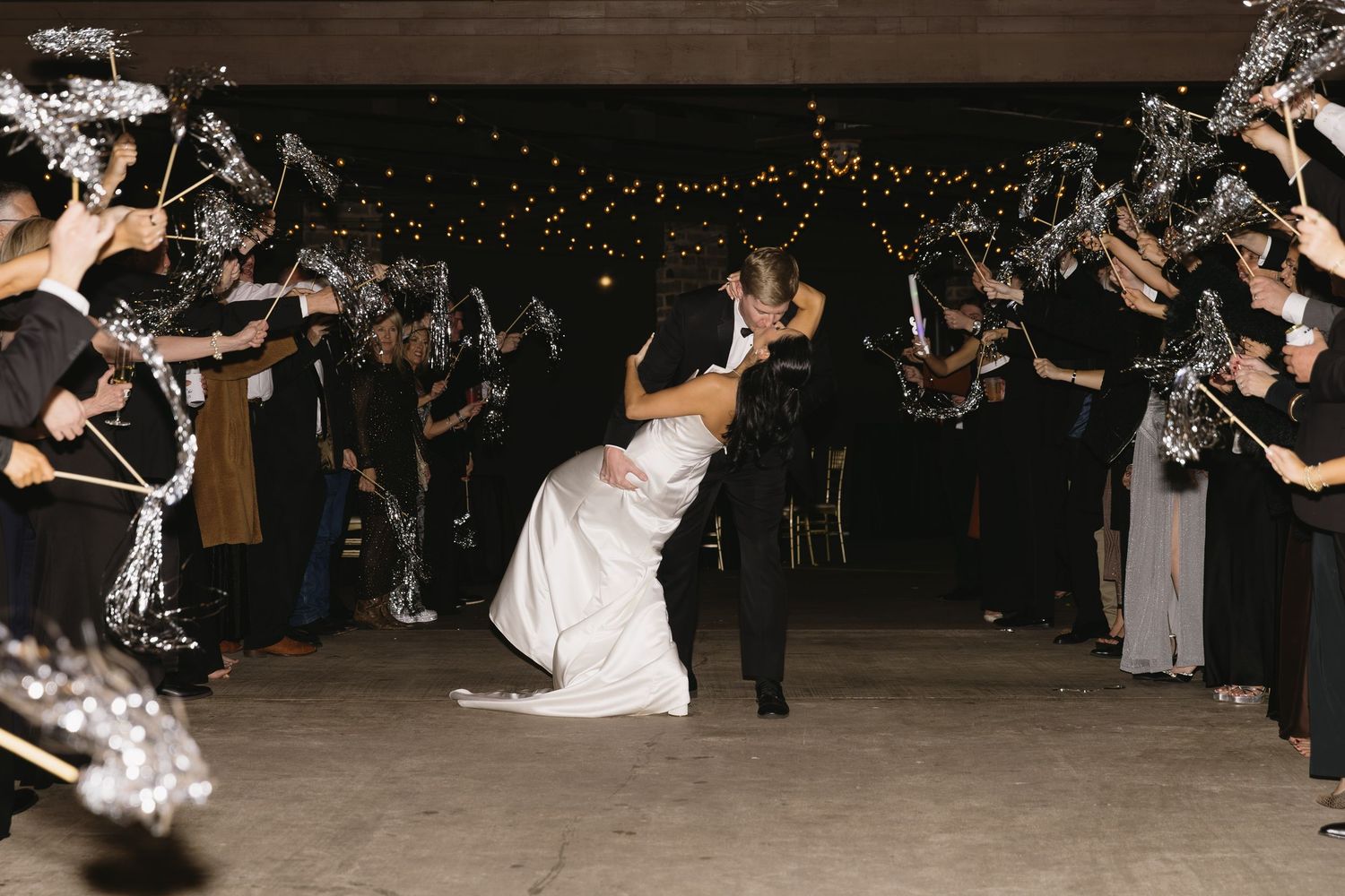 Wedding guests dancing and celebrating on a dark dance floor with string lights overhead.