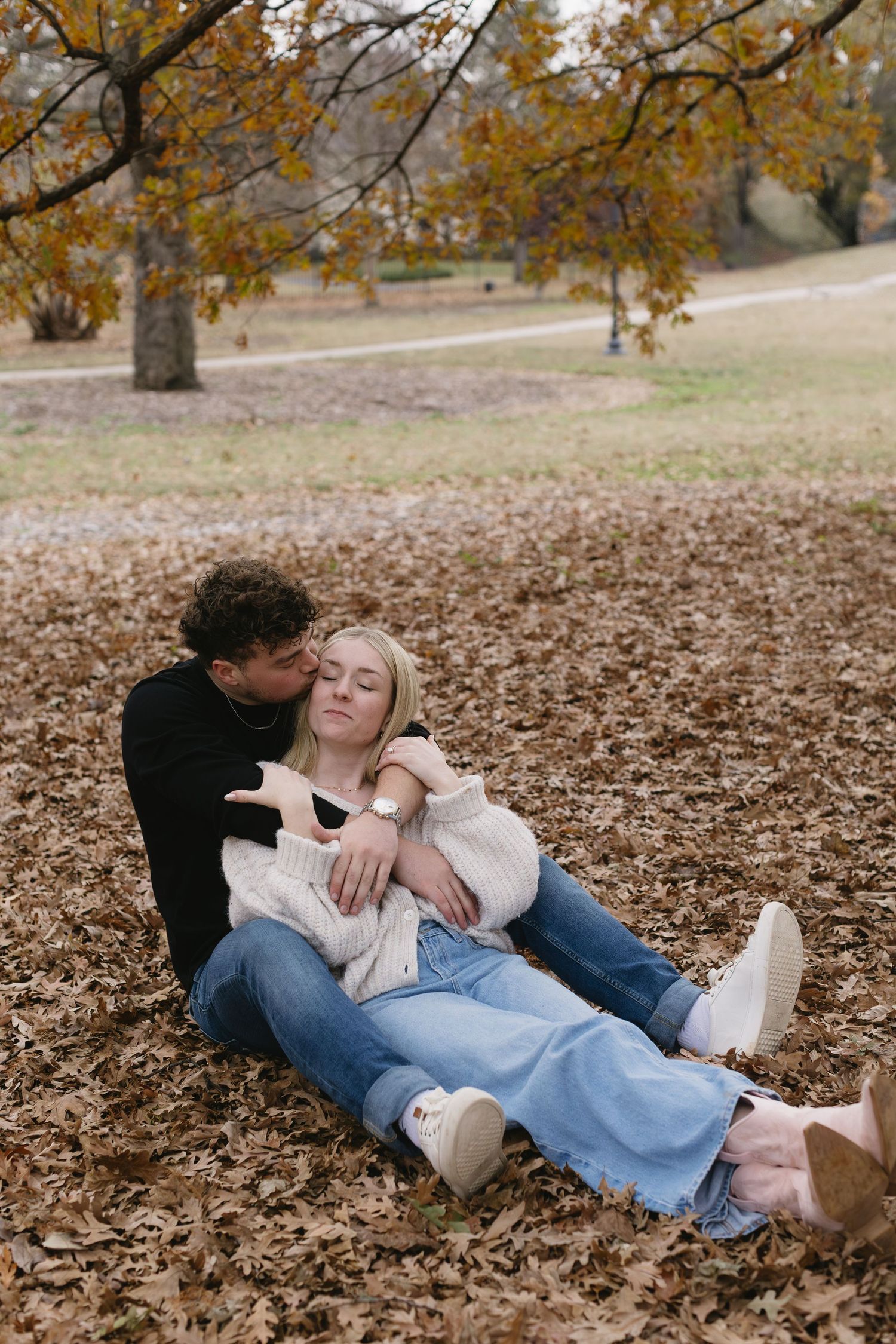 A couple relaxes together on a bed of autumn leaves in a park setting.