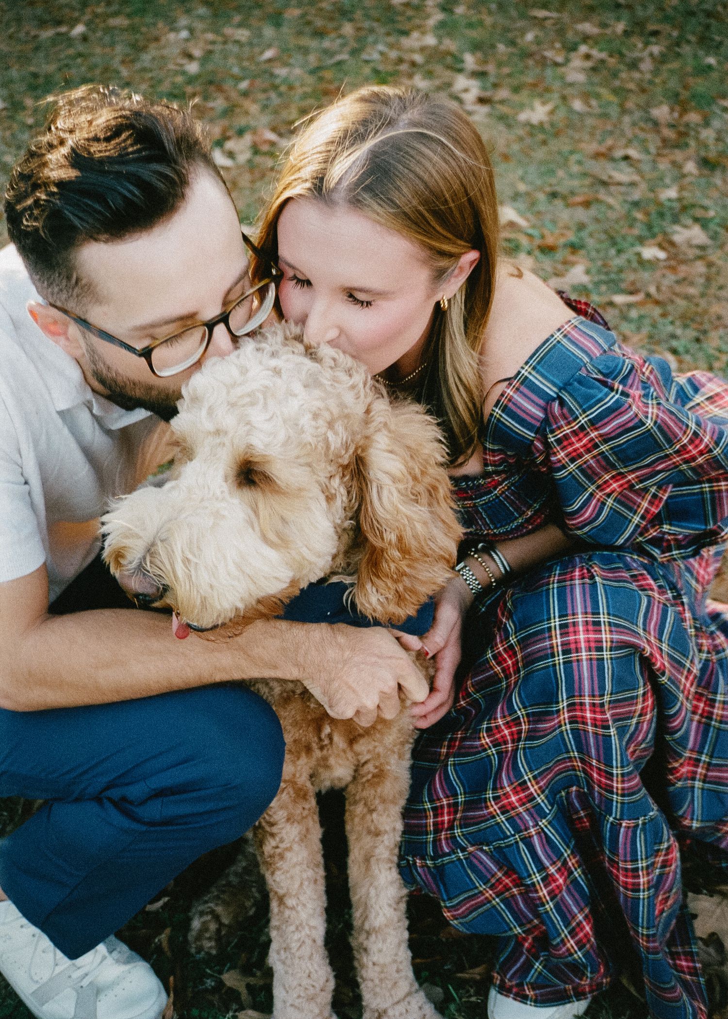 A couple snuggles with their fluffy goldendoodle dog on fallen autumn leaves in a series of candid photos.