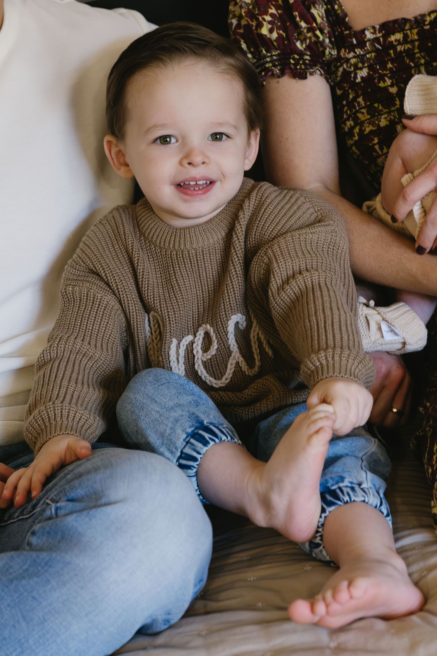 Child wearing brown knit sweater sitting casually on couch.