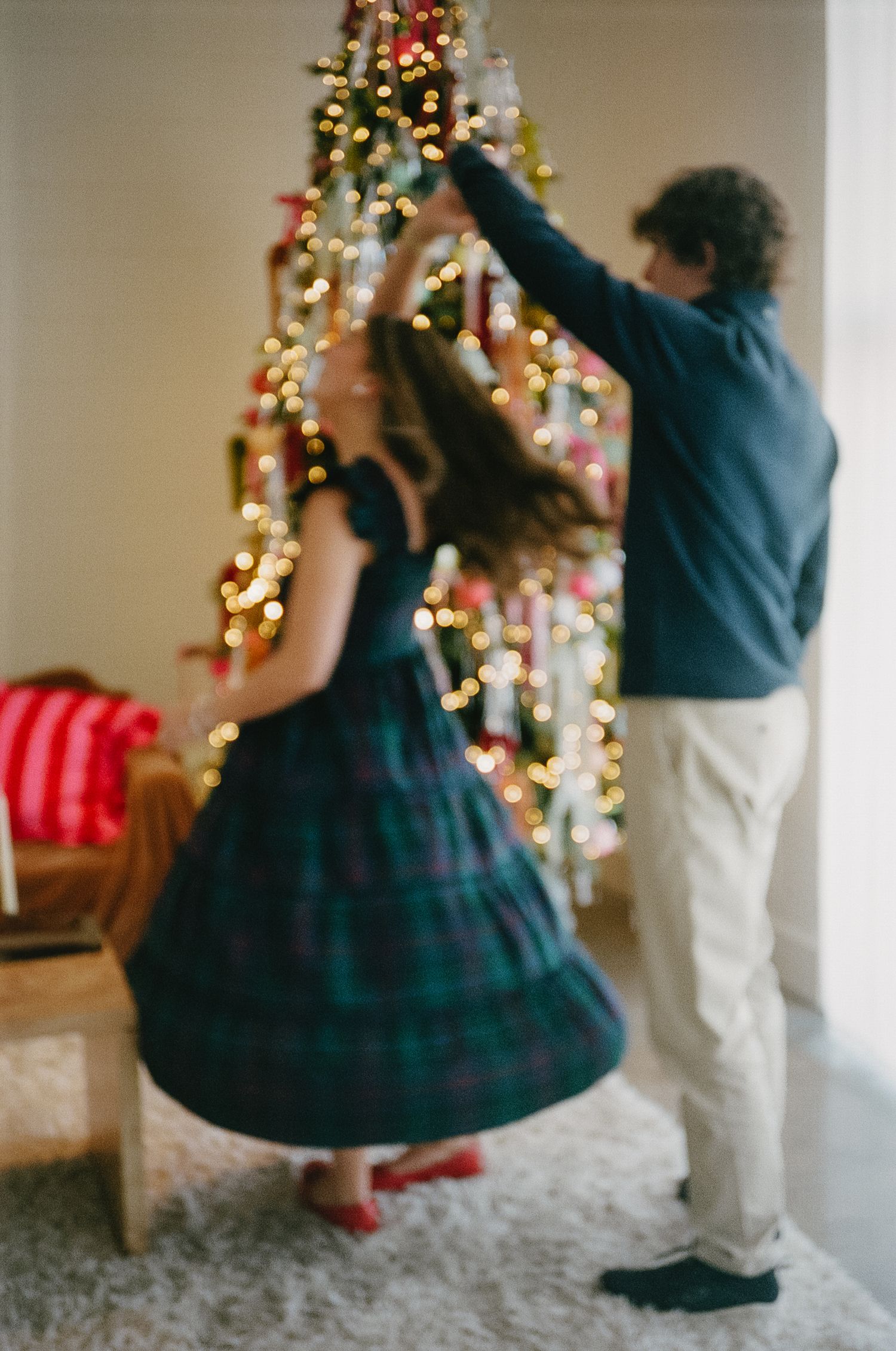 A playful dance scene unfolds in front of a glowing Christmas tree with someone in a navy dress twirling.