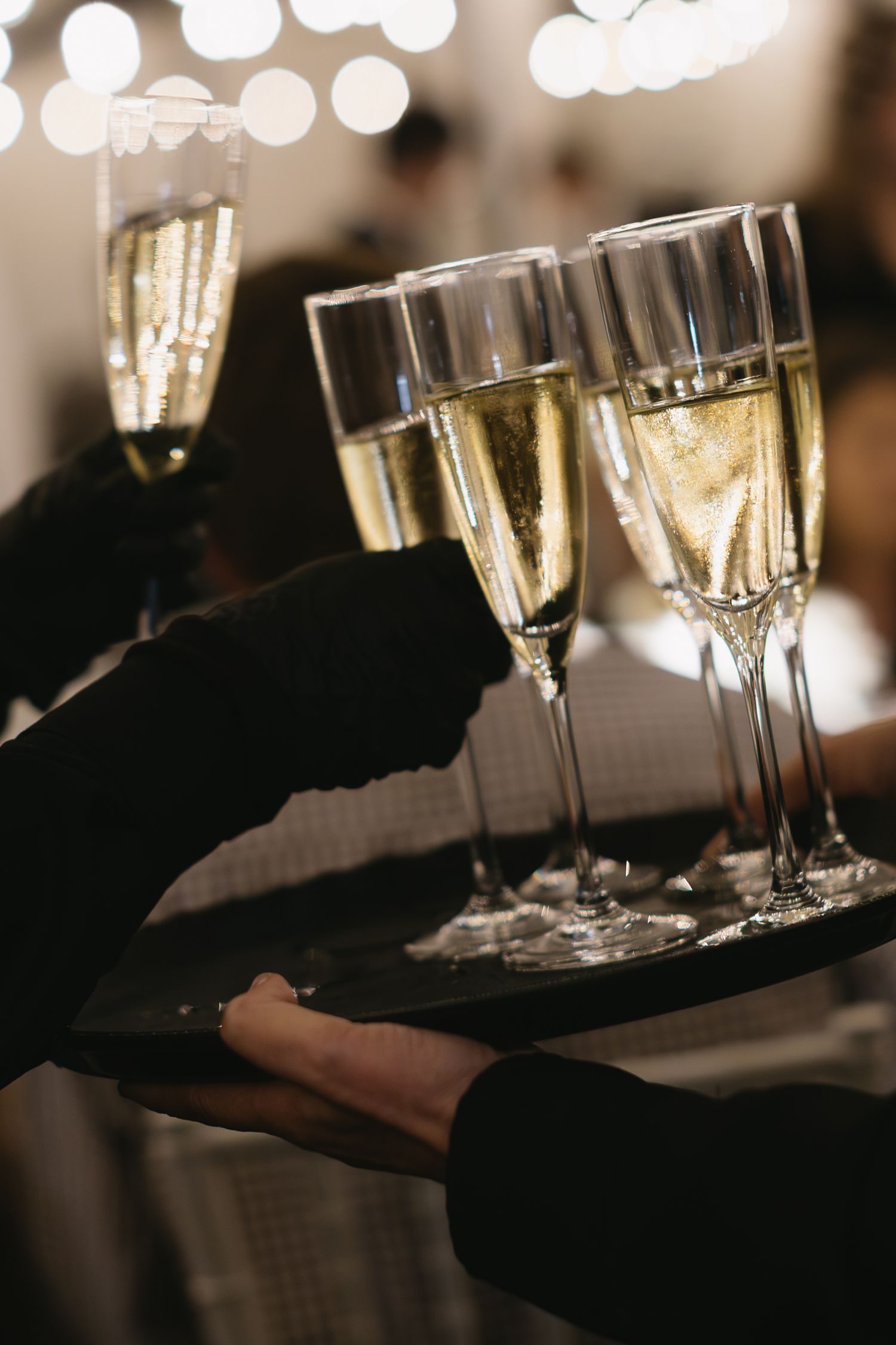 Champagne glasses on serving trays with bokeh lighting effects in dark reception setting.