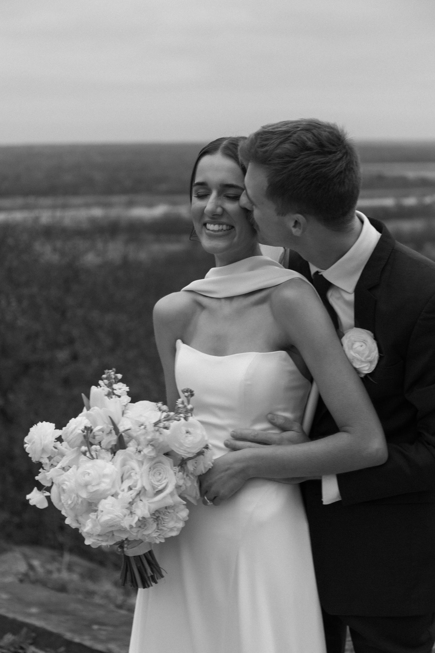 Black and white wedding portraits showing tender moments between newlyweds with white flowers.