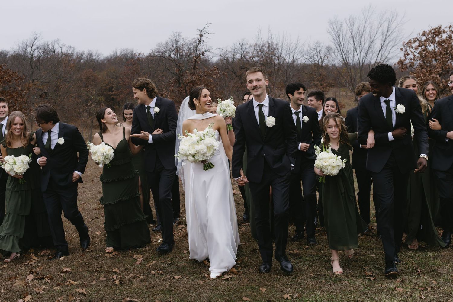 Wedding party in black and white attire walking through an autumn field.