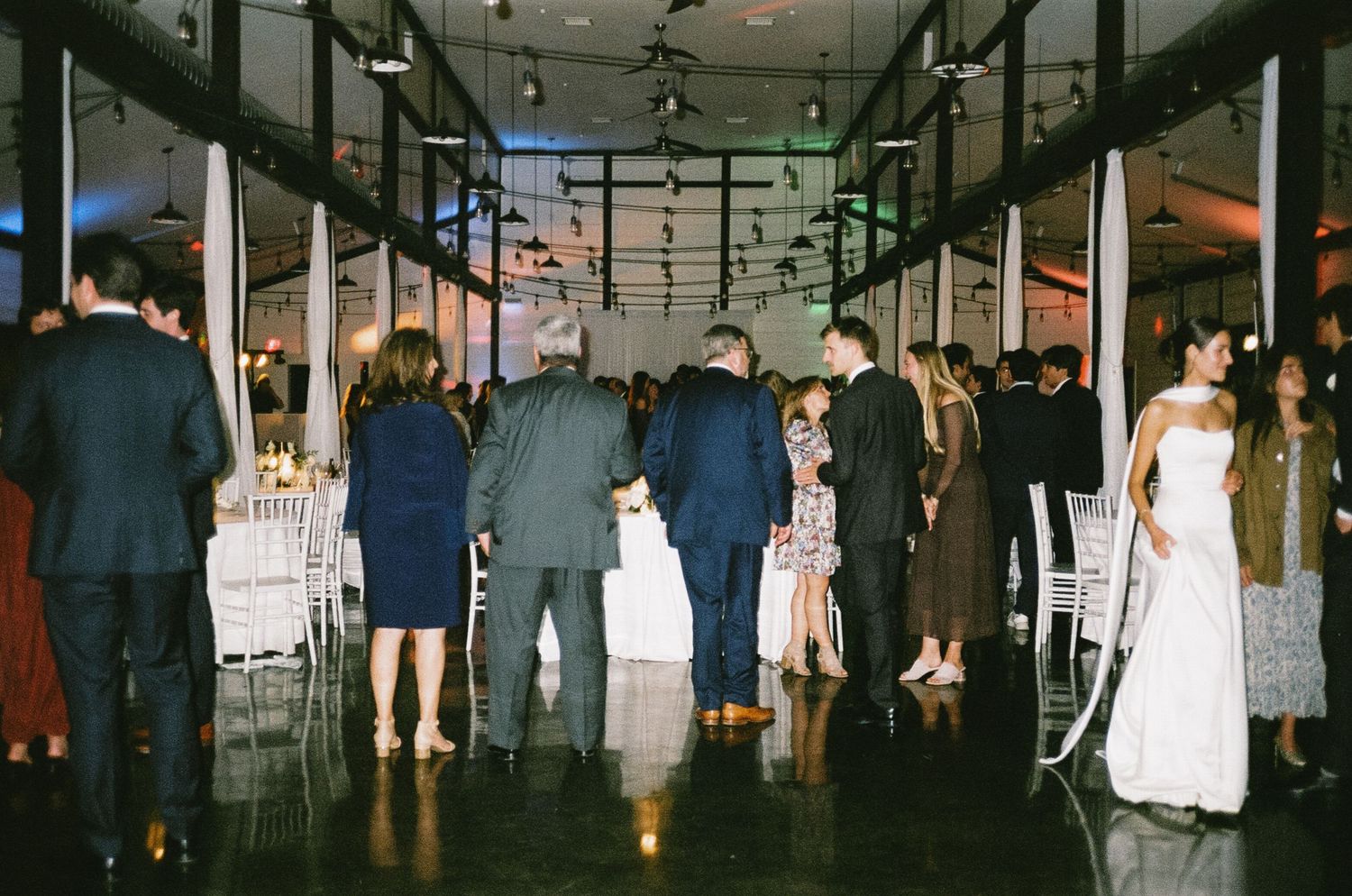 Wedding reception venue with dimmed lighting and guests mingling in formal attire.