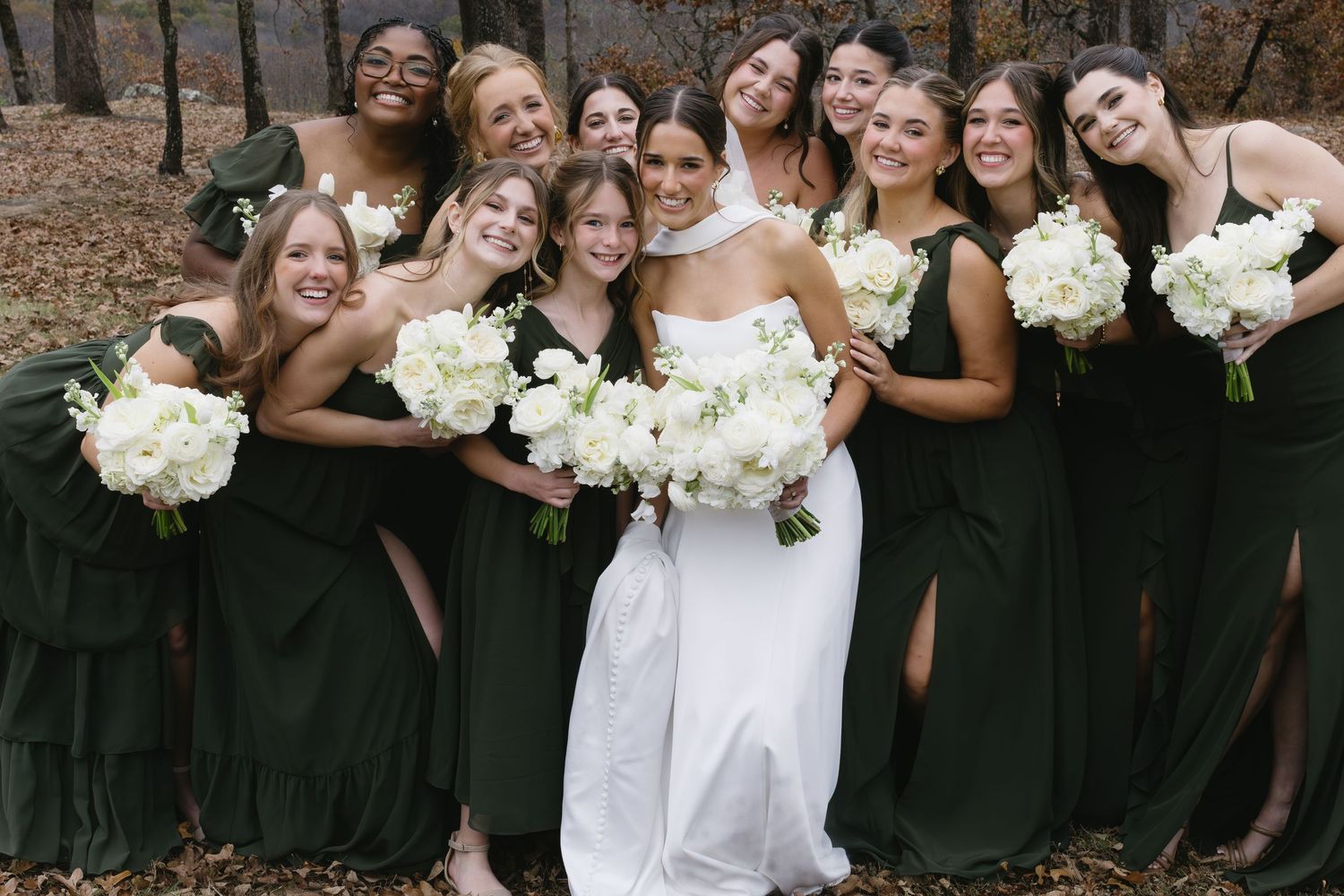 Wedding party in black attire poses with bride in white holding matching bouquets.