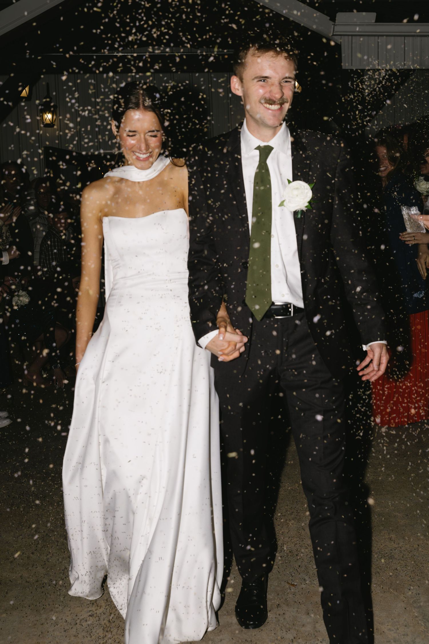 Newlyweds walking through falling snow at night after their winter wedding celebration.