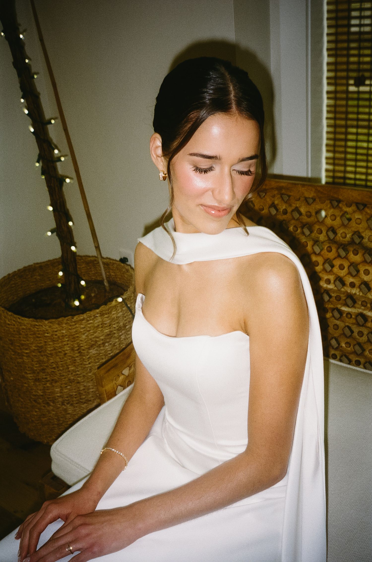 Bride in an elegant white wedding dress seated in a room with twinkling lights.
