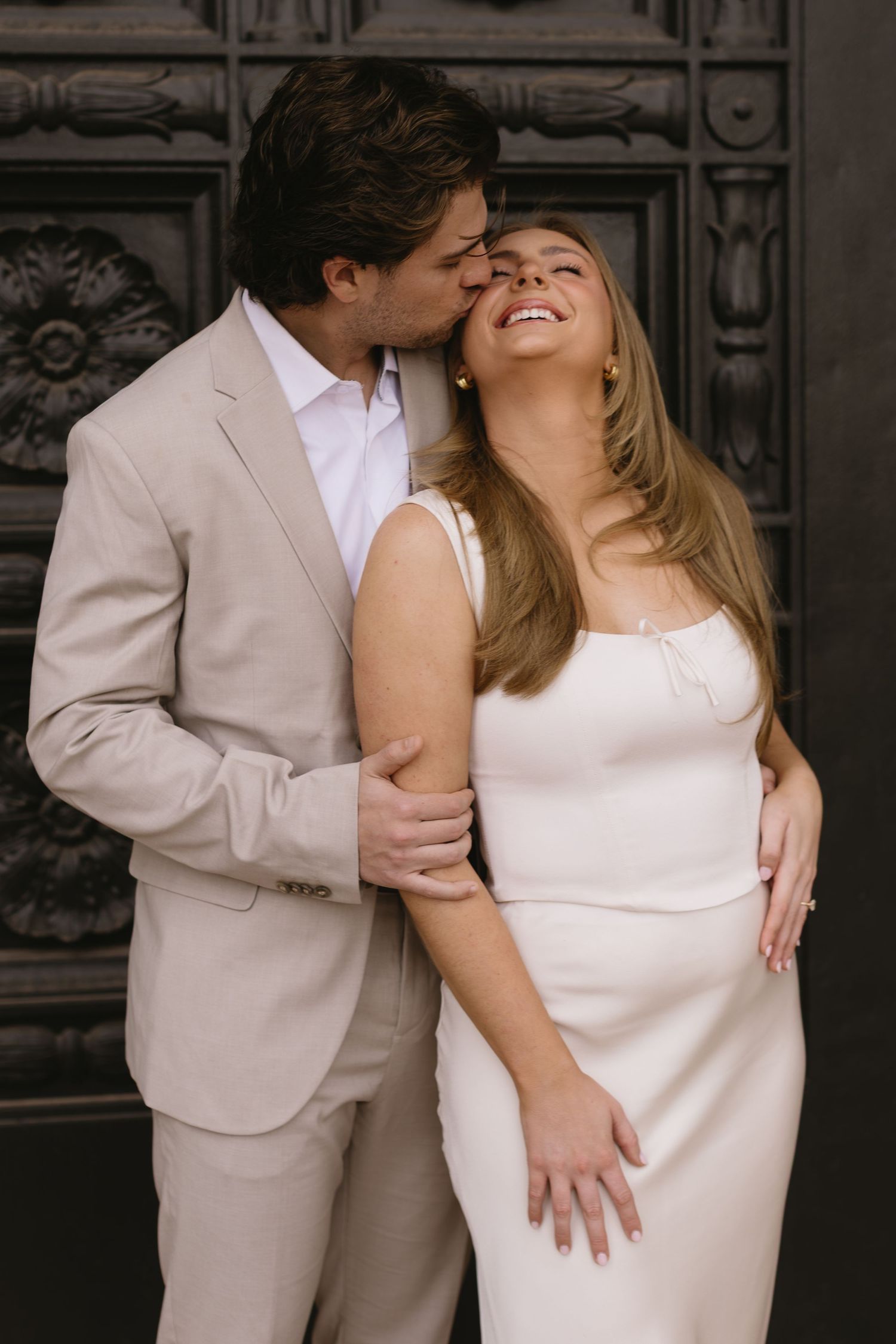 Romantic couple in matching white and beige outfits embrace in a series of intimate poses against a dark background.