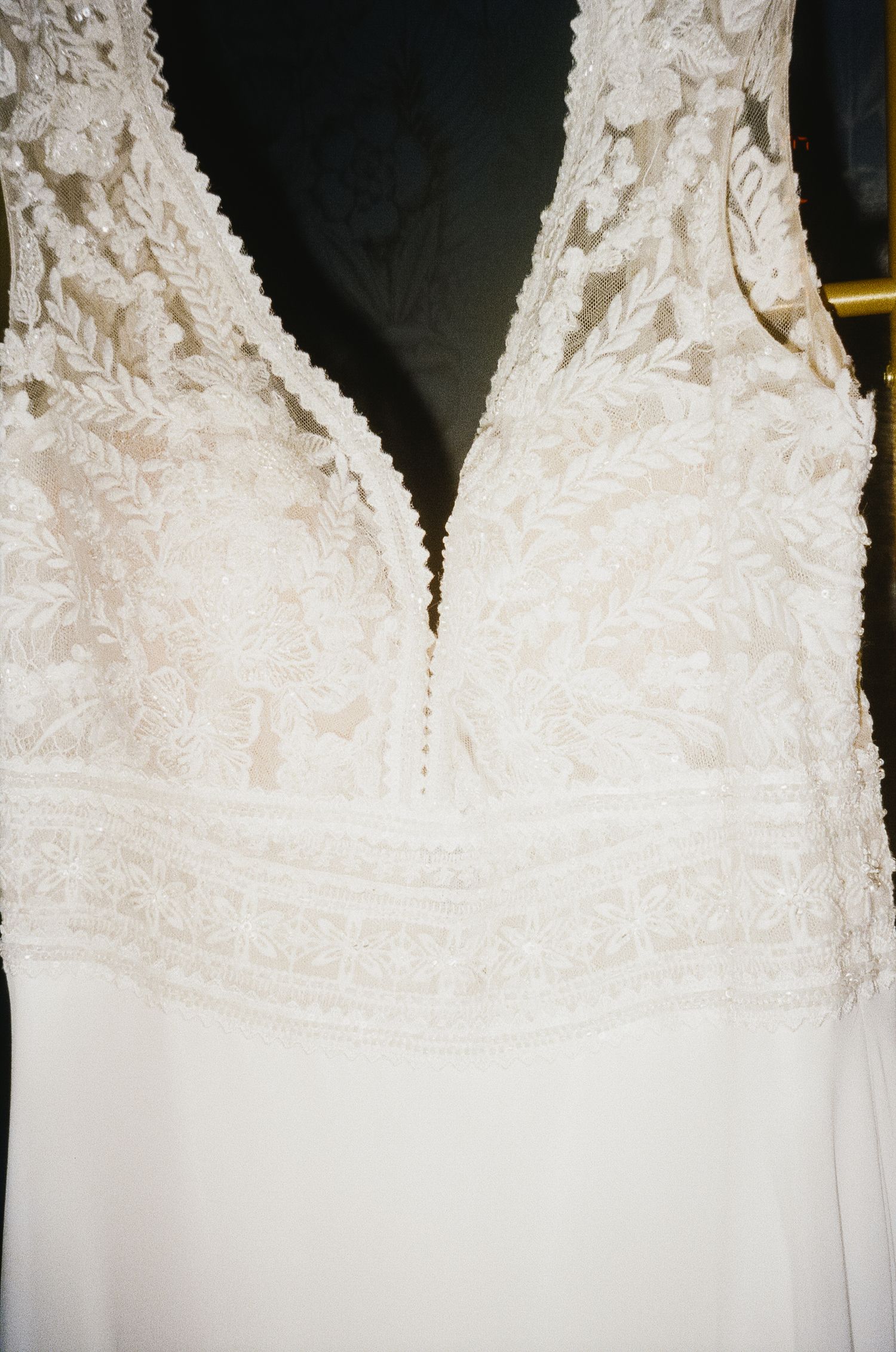 Close-up details of white lace wedding dresses with intricate embroidery patterns hanging on display.