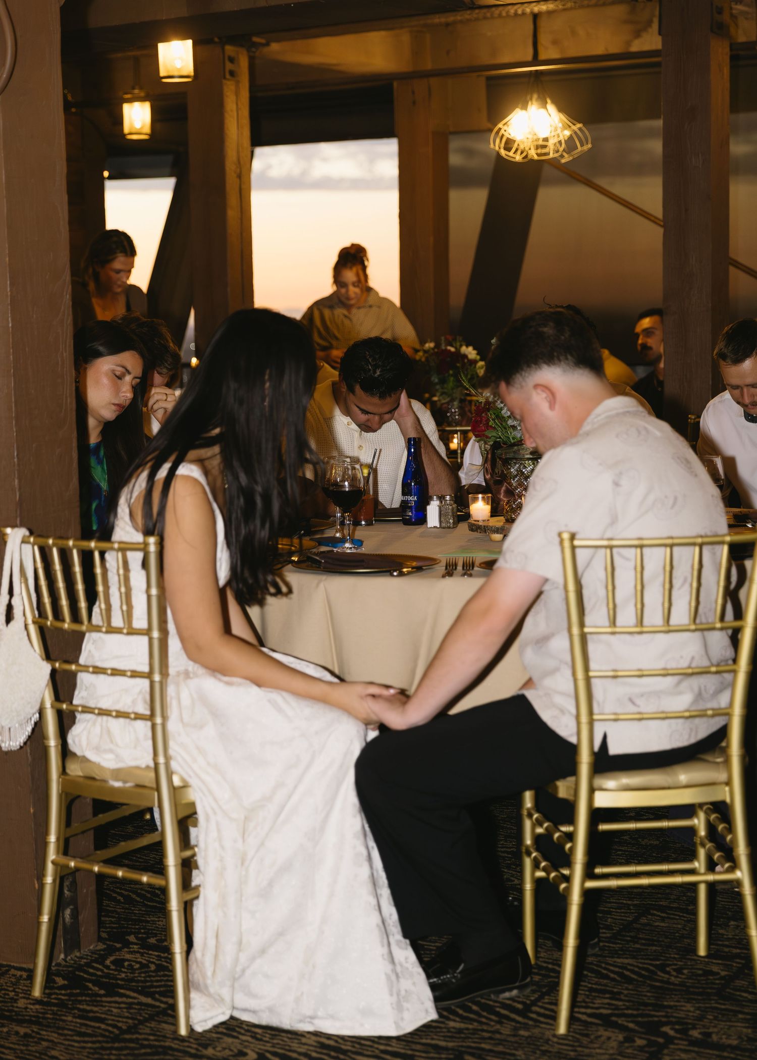 Wedding reception guests seated at elegant tables with gold chairs in a dimly lit banquet hall.