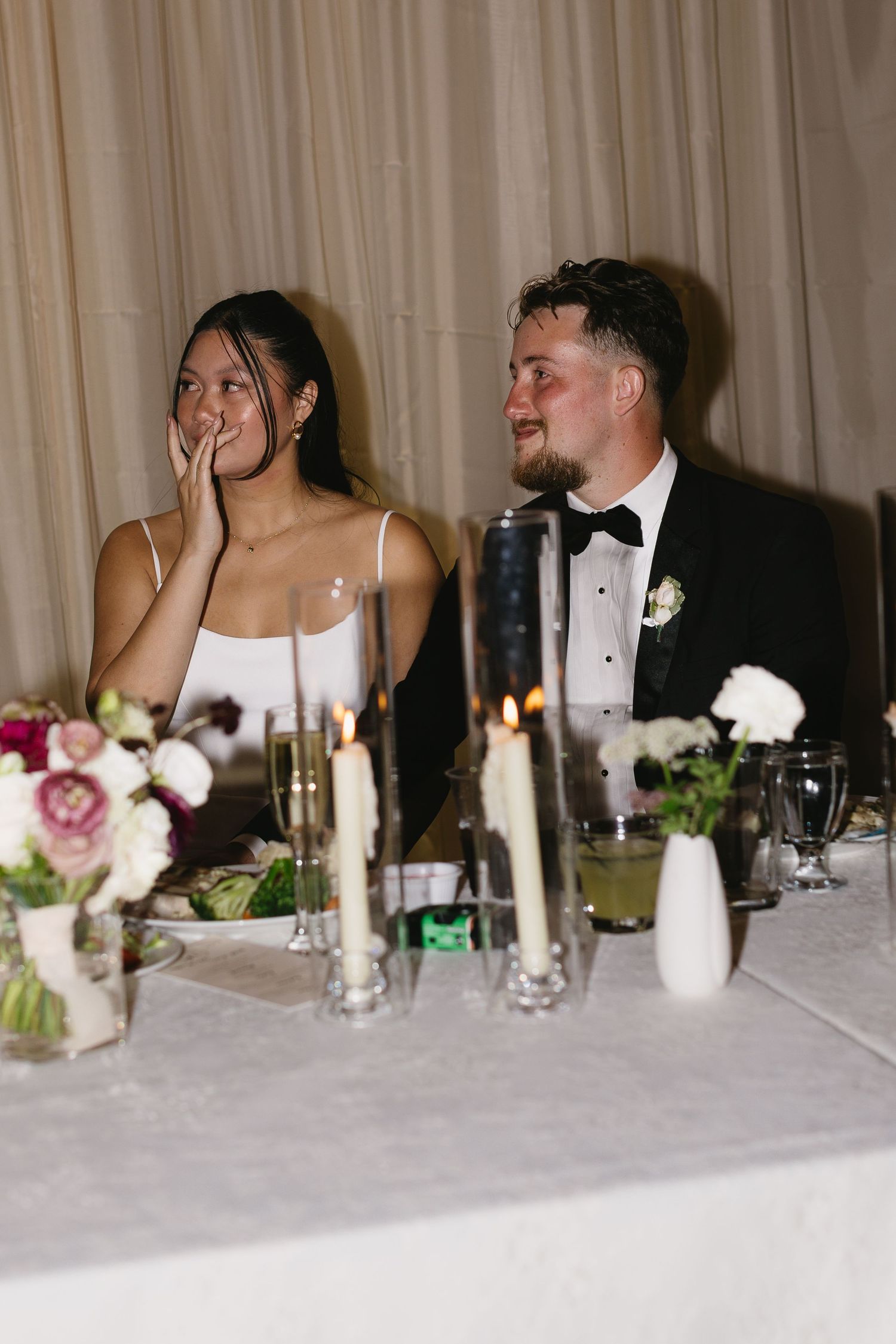 Candid moments at wedding reception head table with white linens and candlelight.