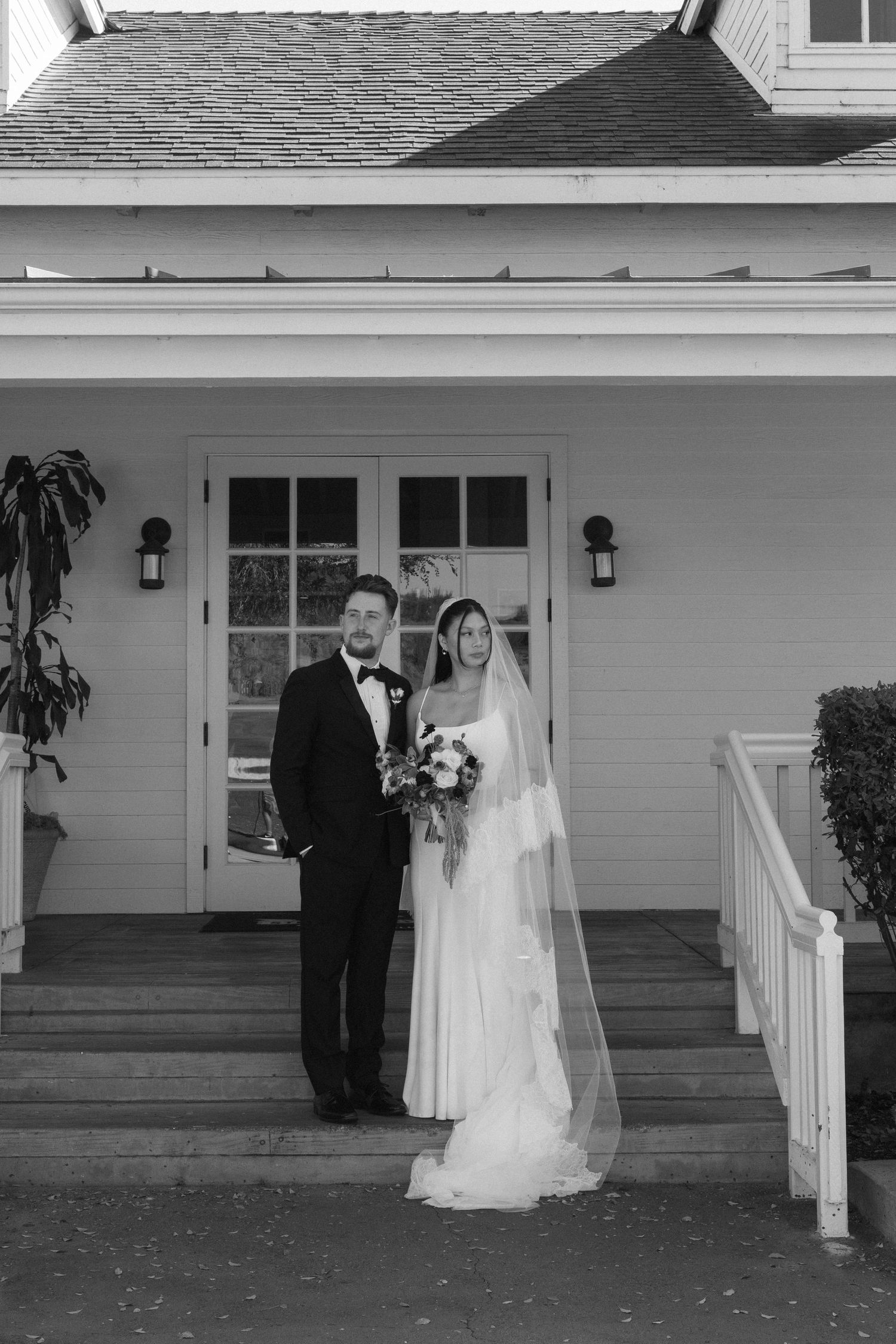 Black and white photo of newlyweds standing on porch of white house.