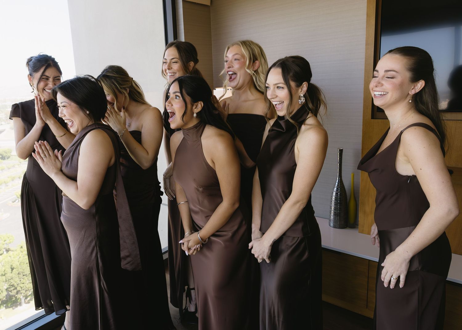 Group of bridesmaids in brown dresses gathered together indoors.