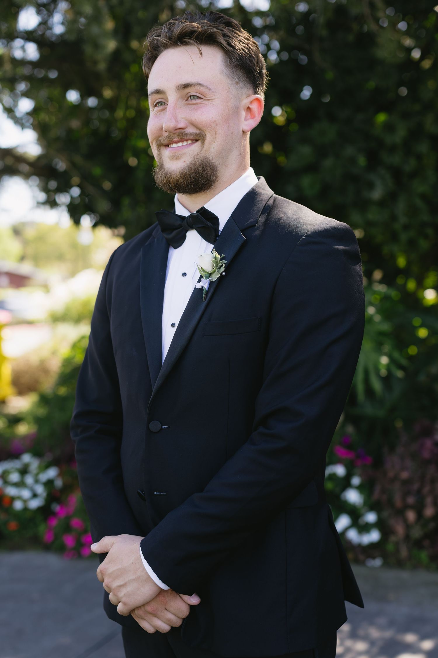 Groom in classic black tuxedo smiles during outdoor wedding portraits.