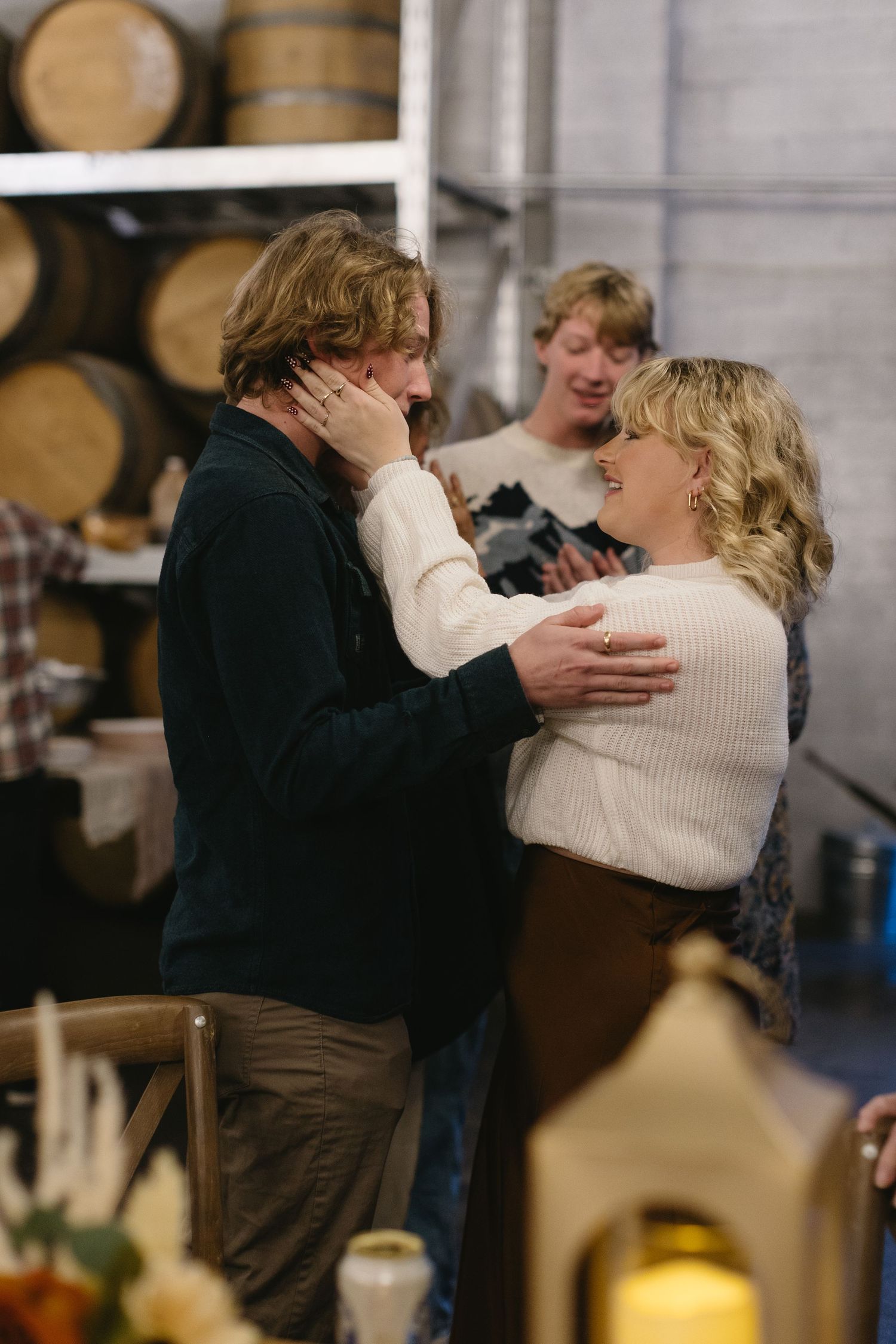 Emotional moment shared between people at a rustic venue with wine barrels in background.