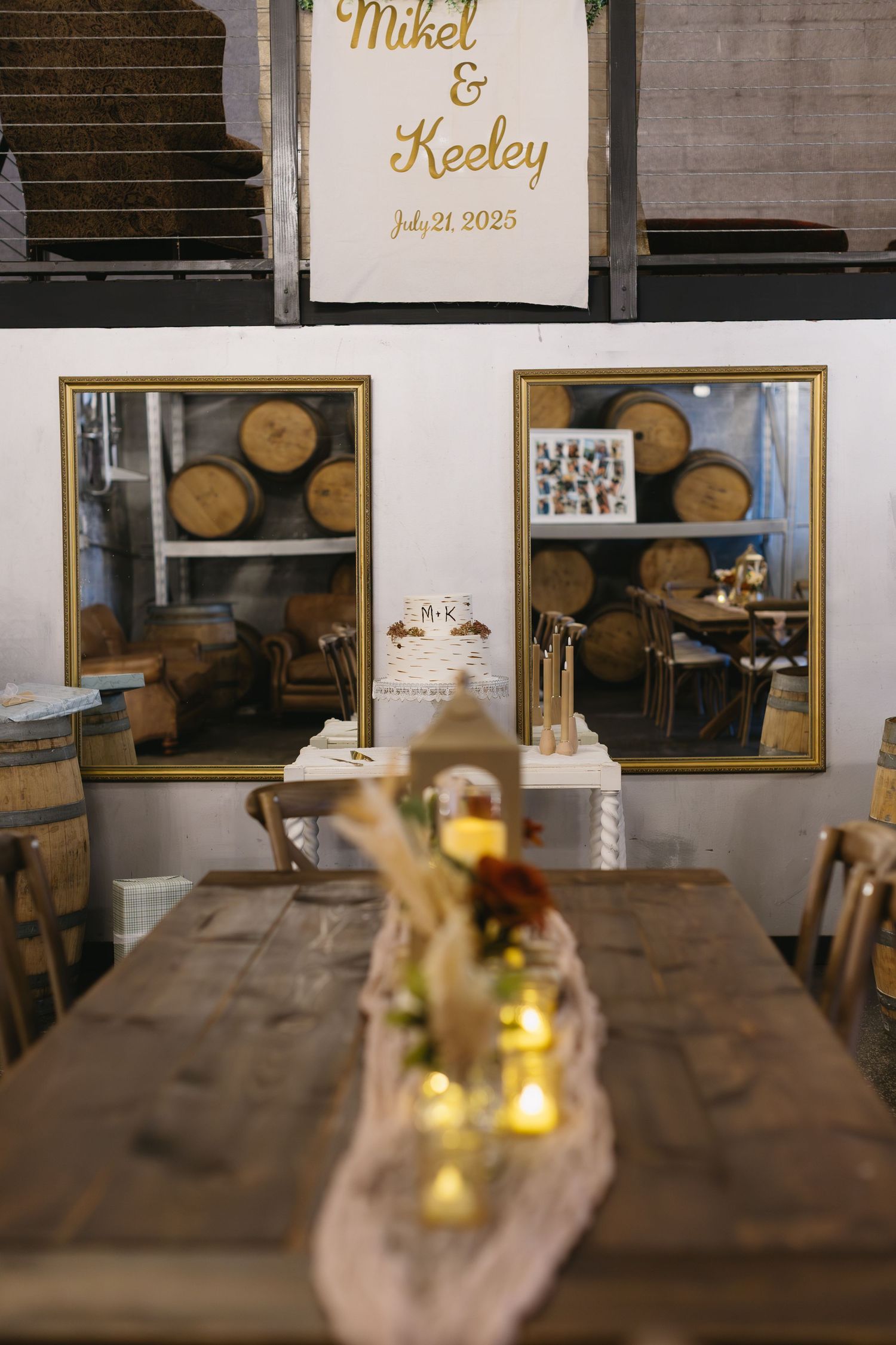 Rustic wedding reception table with wooden barrels and mirrors in background, decorated with candlelit centerpieces.