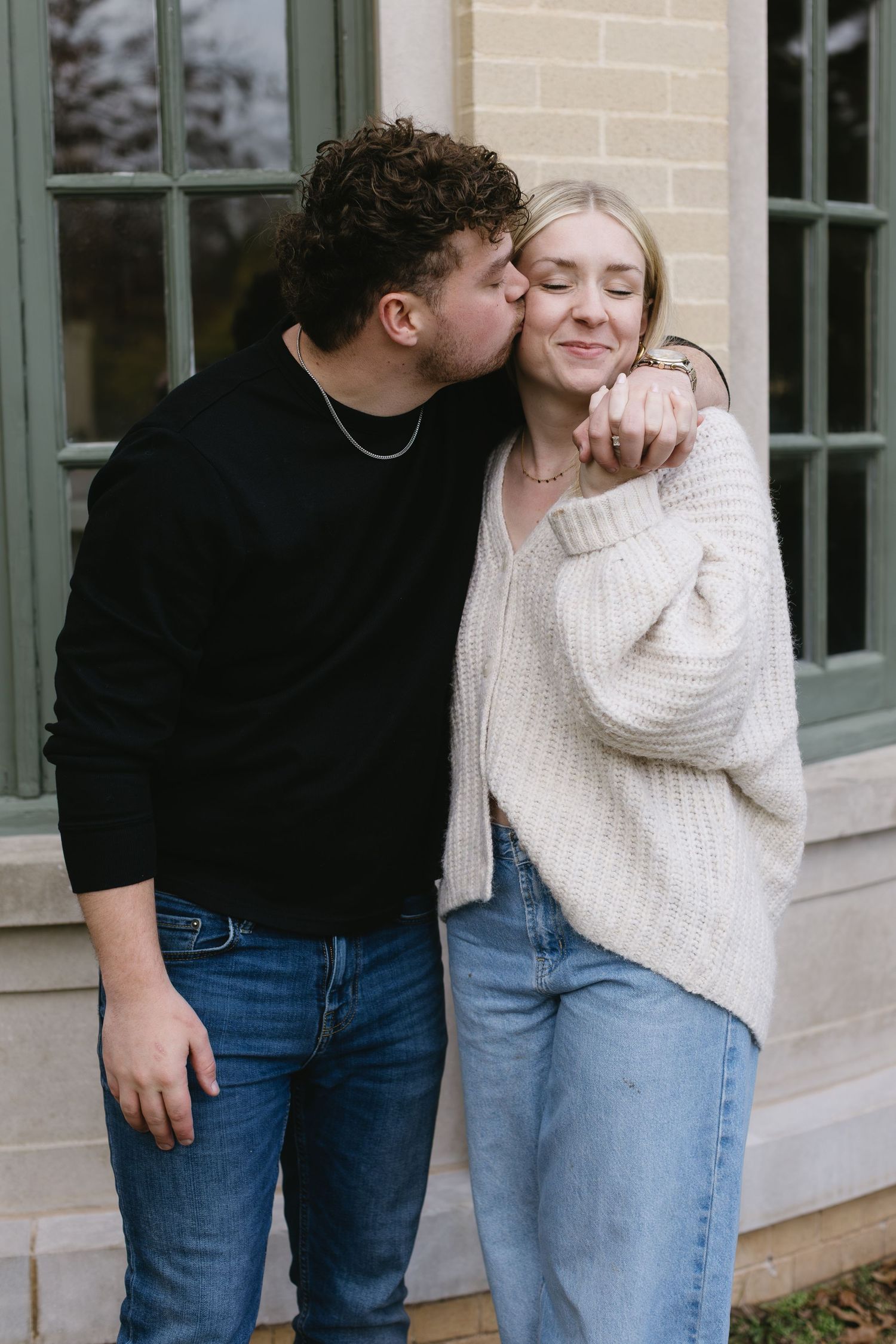 Couple in matching jeans and sweaters share an intimate moment against a beige wall.