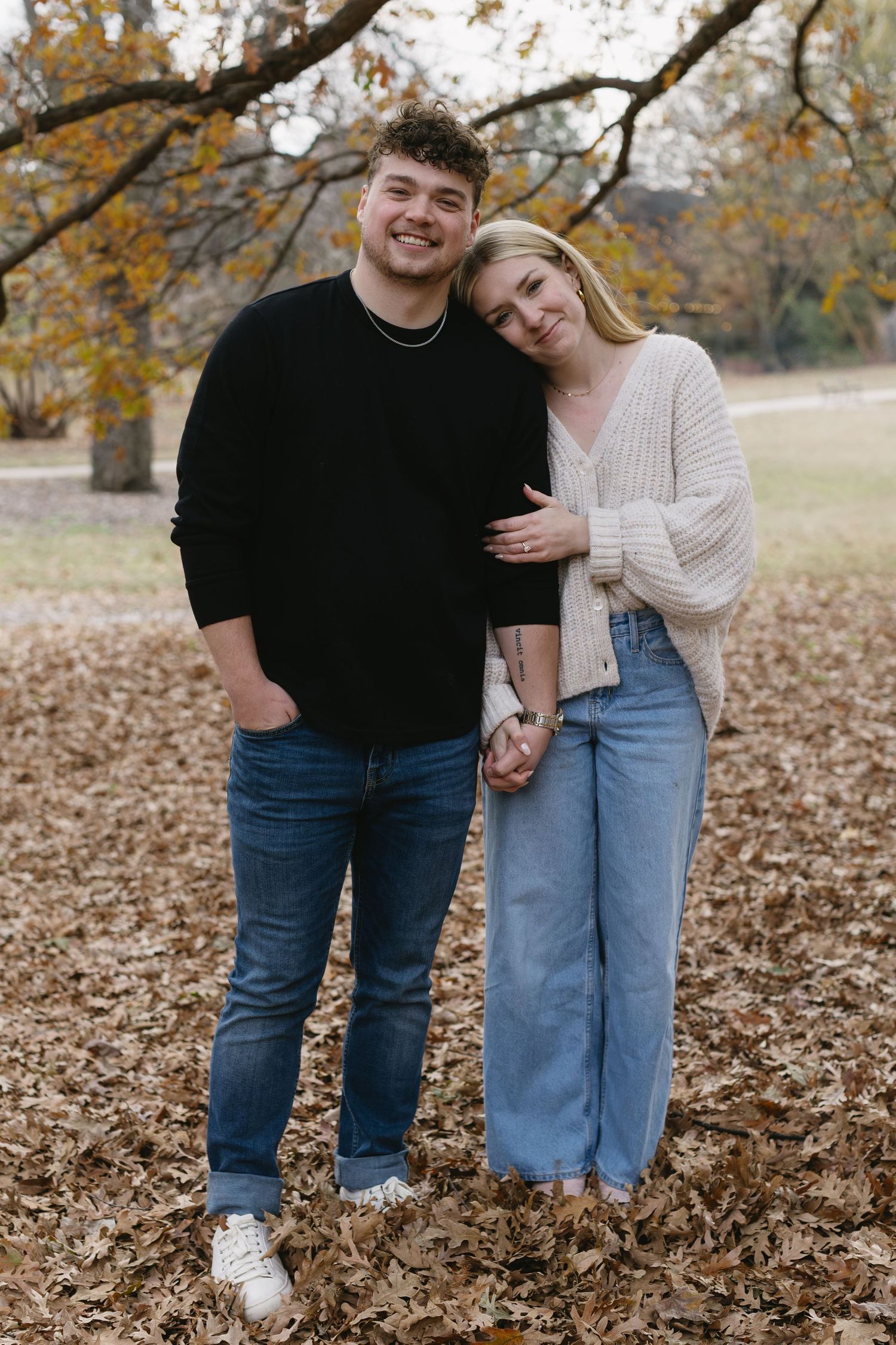 A couple stands close together on fallen leaves during a fall outdoor photo session.