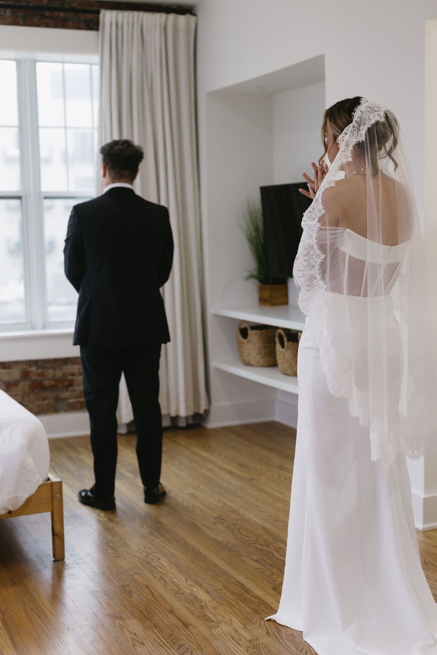First look wedding moment in bright room with hardwood floors and white curtains.