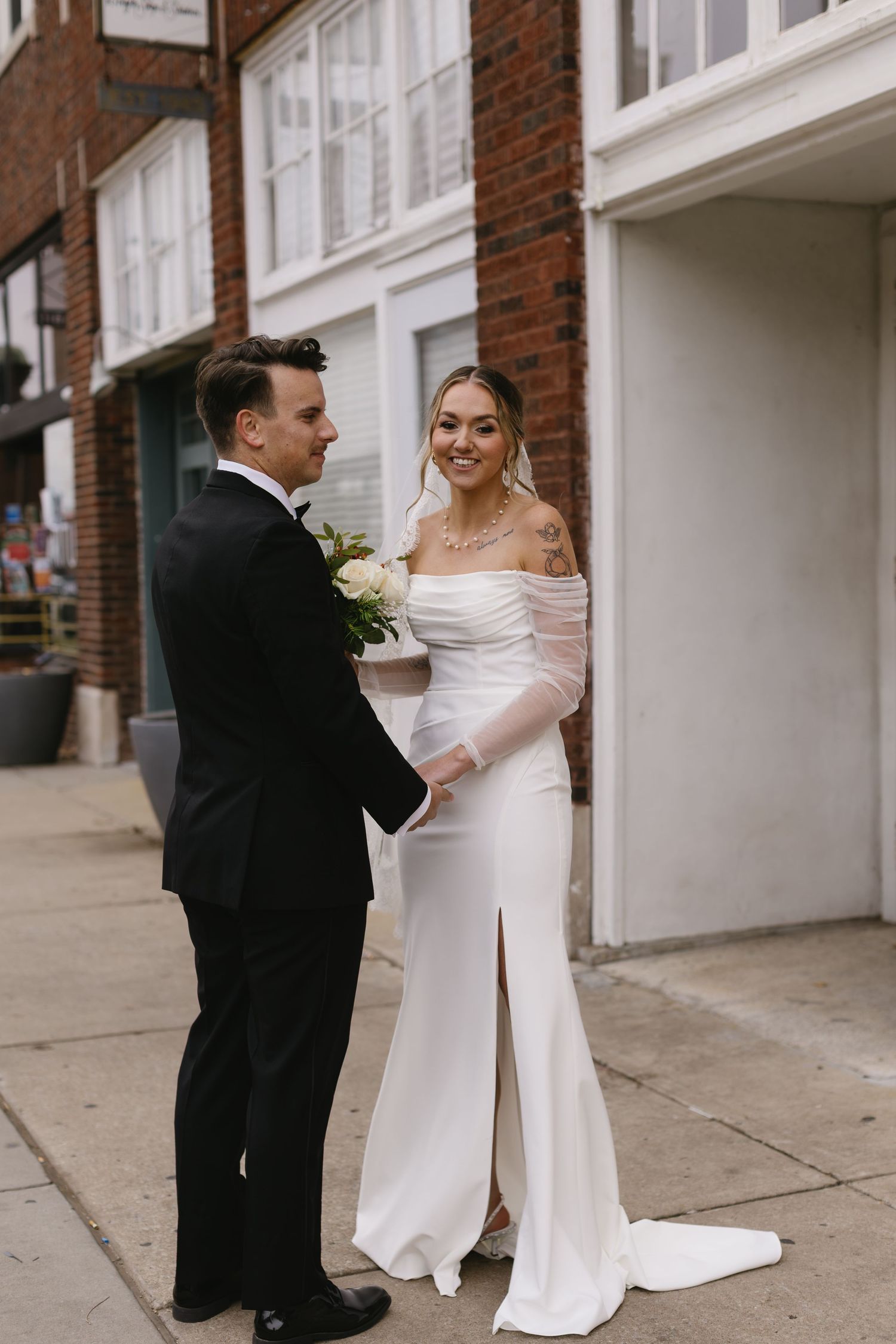 Couple in wedding attire sharing a moment on a brick-lined street.