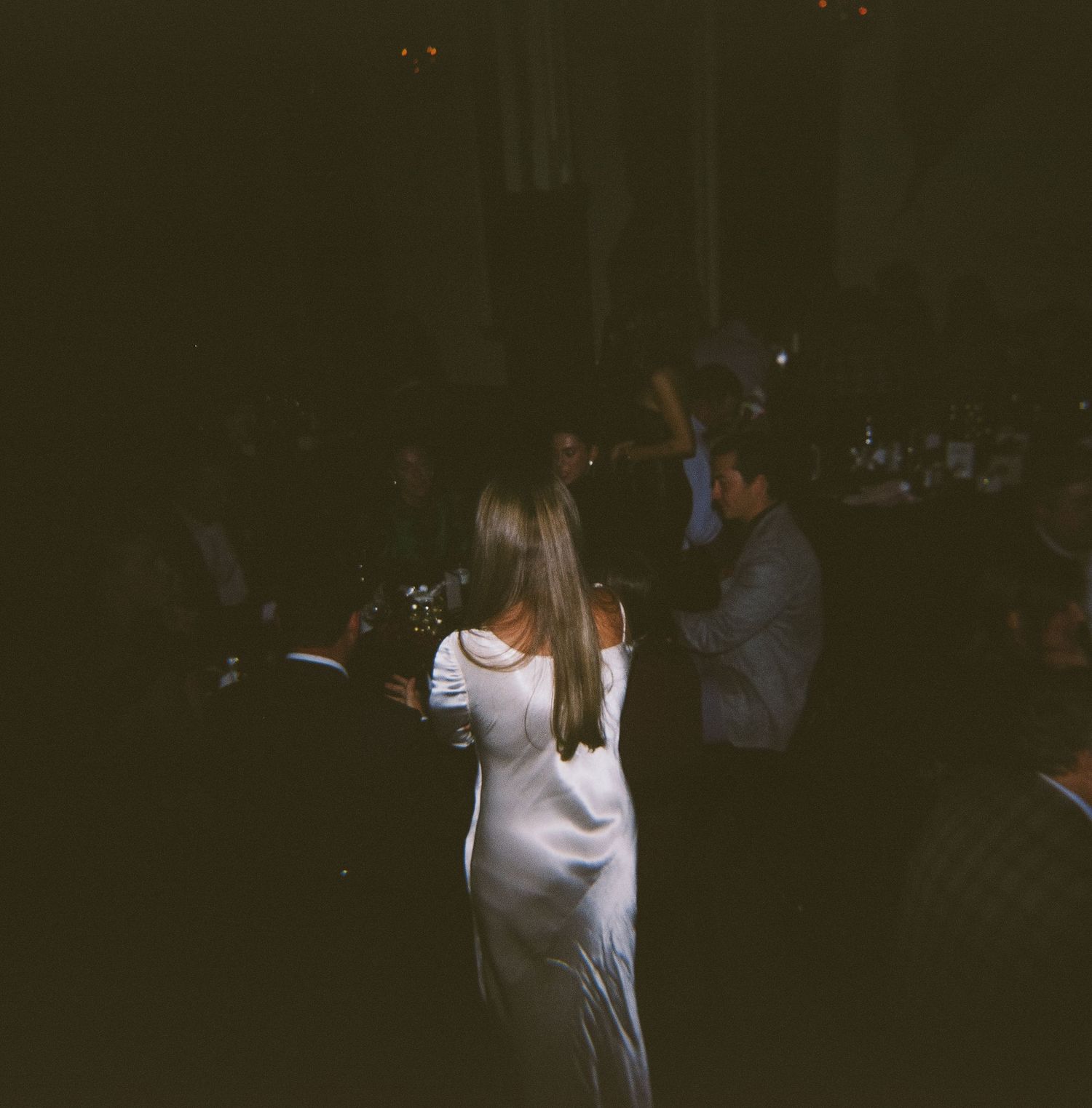 Wedding guests dancing in a dimly lit reception venue with festive lighting.
