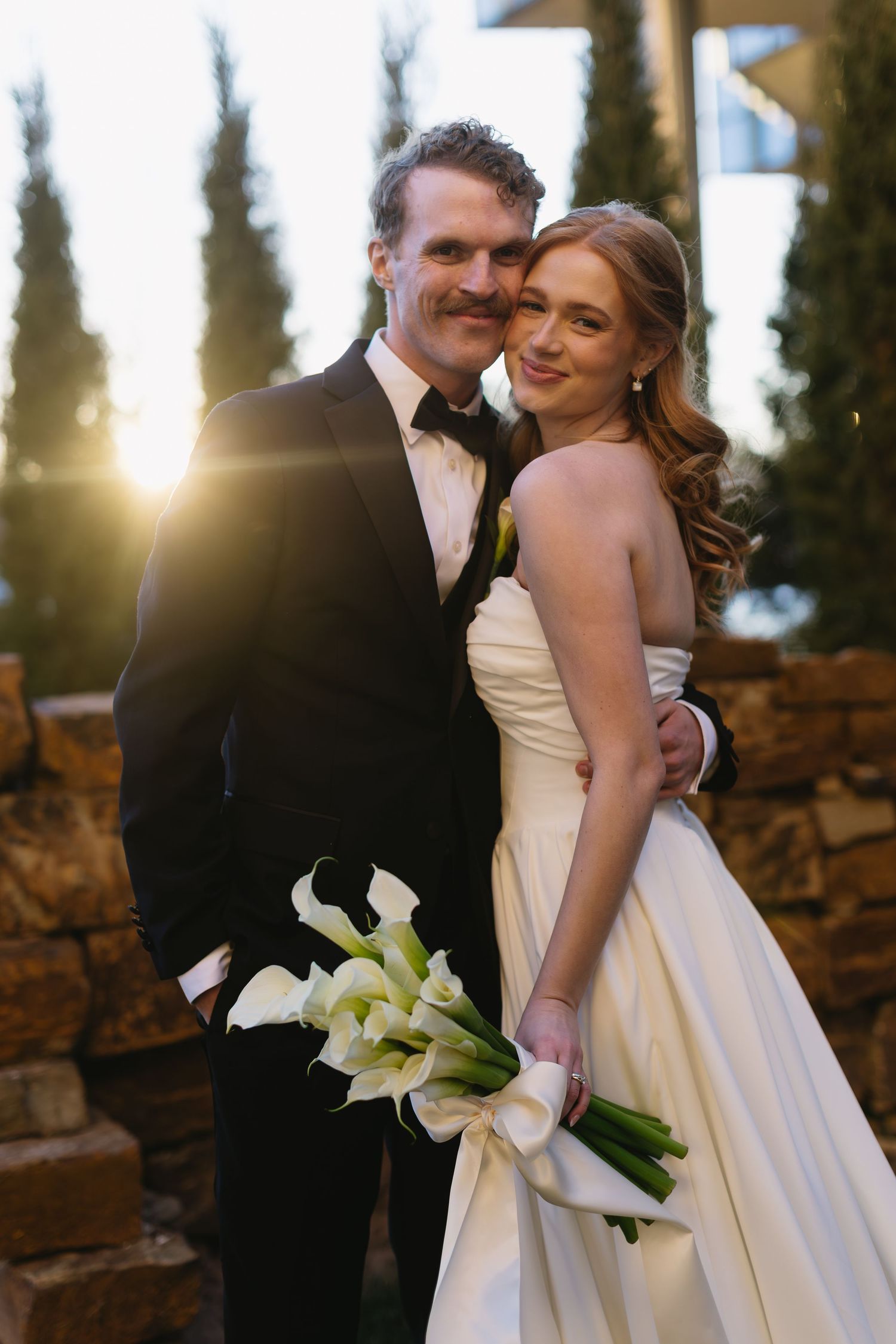A wedding couple shares a romantic moment at sunset with calla lily bouquet.