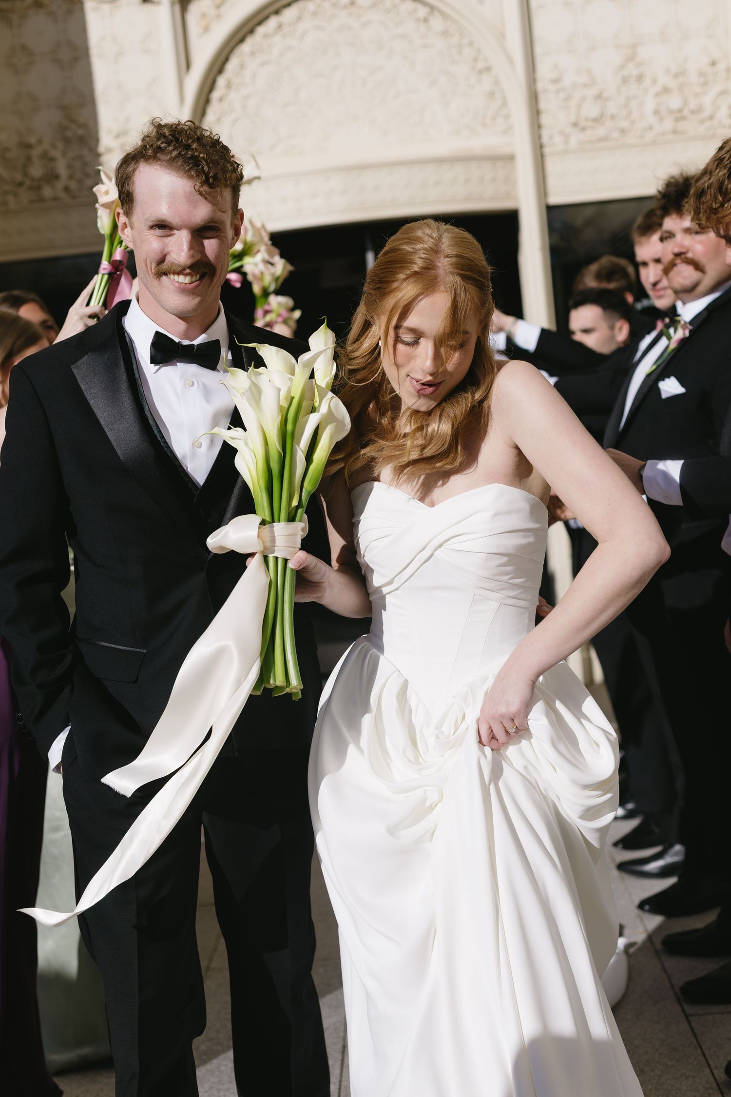 Bridal party in white and black formal attire poses together during wedding celebration.