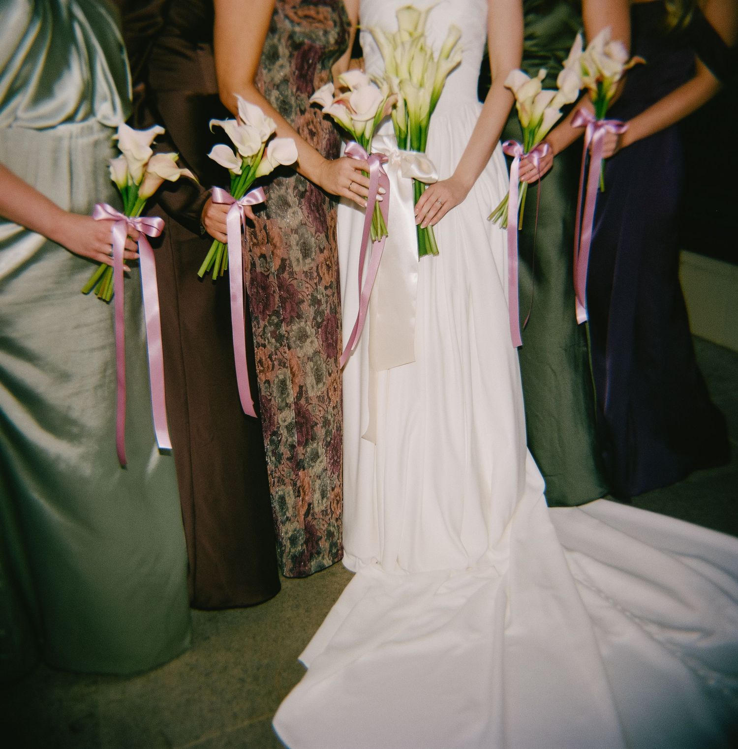 Bridesmaids holding pink and white lily bouquets with ribbon accents.