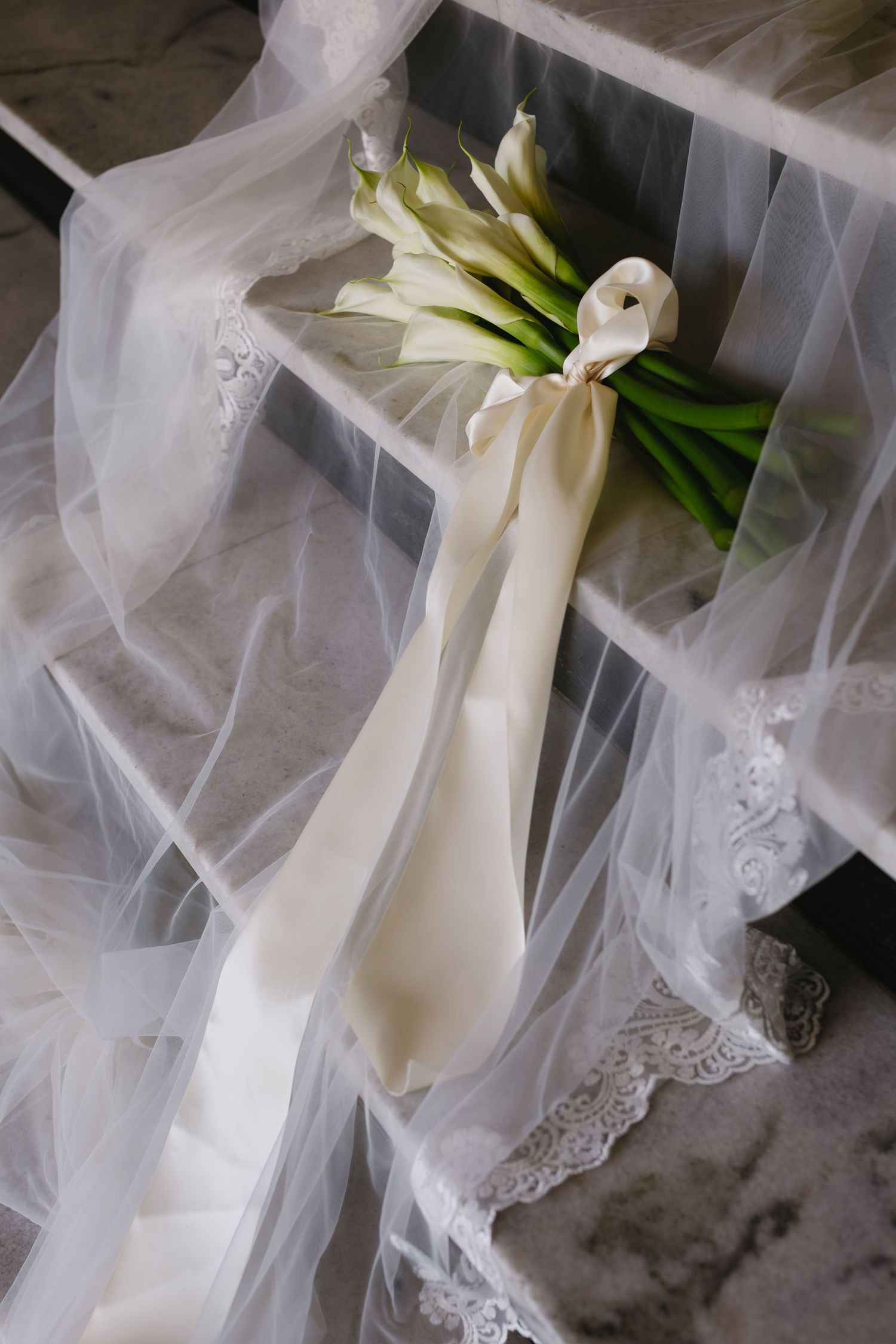 White wedding bouquet wrapped in delicate lace and tulle veil fabric against a marble background.