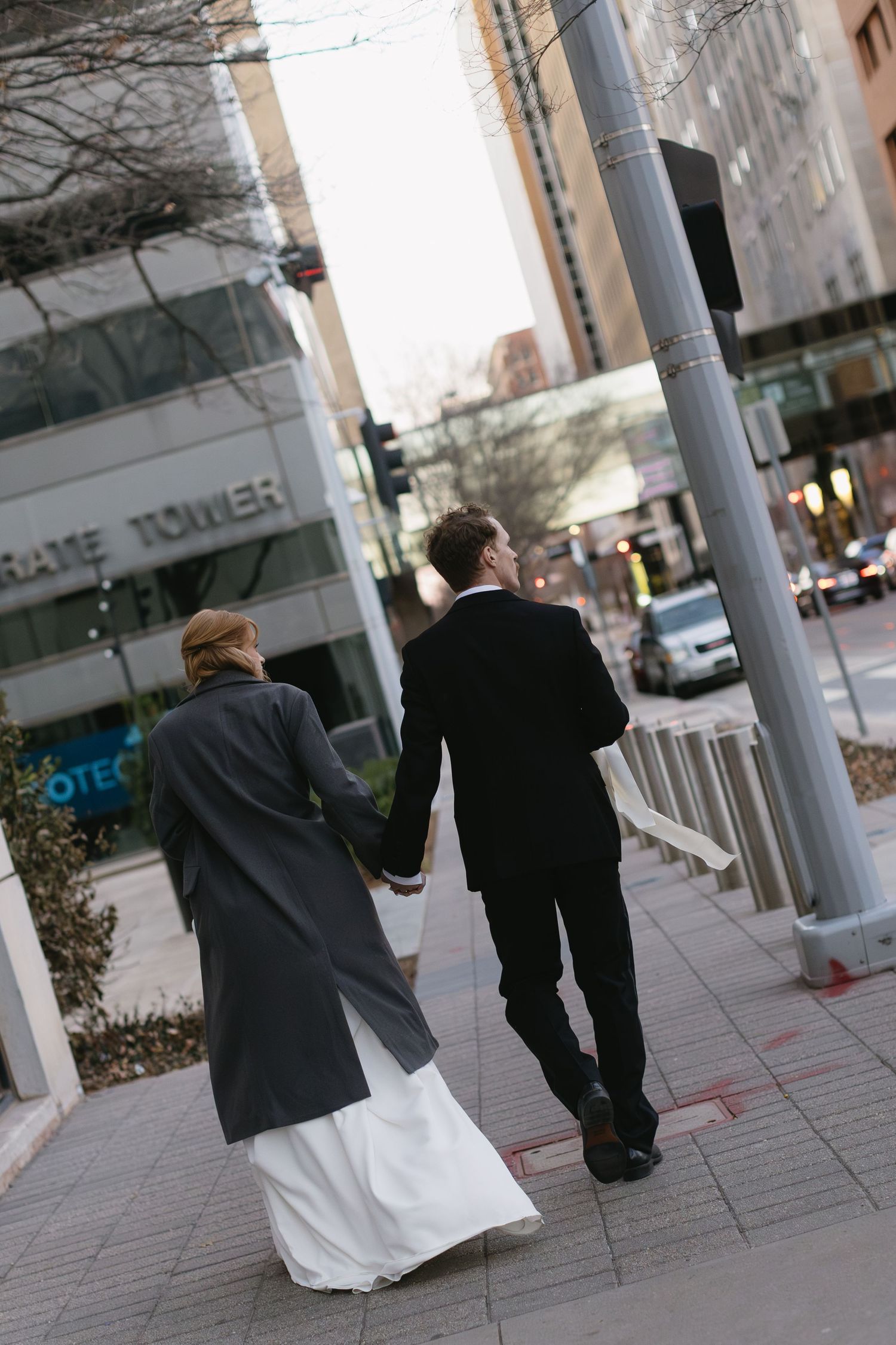 Two people walking down a city sidewalk with one wearing a white dress and dark jacket.