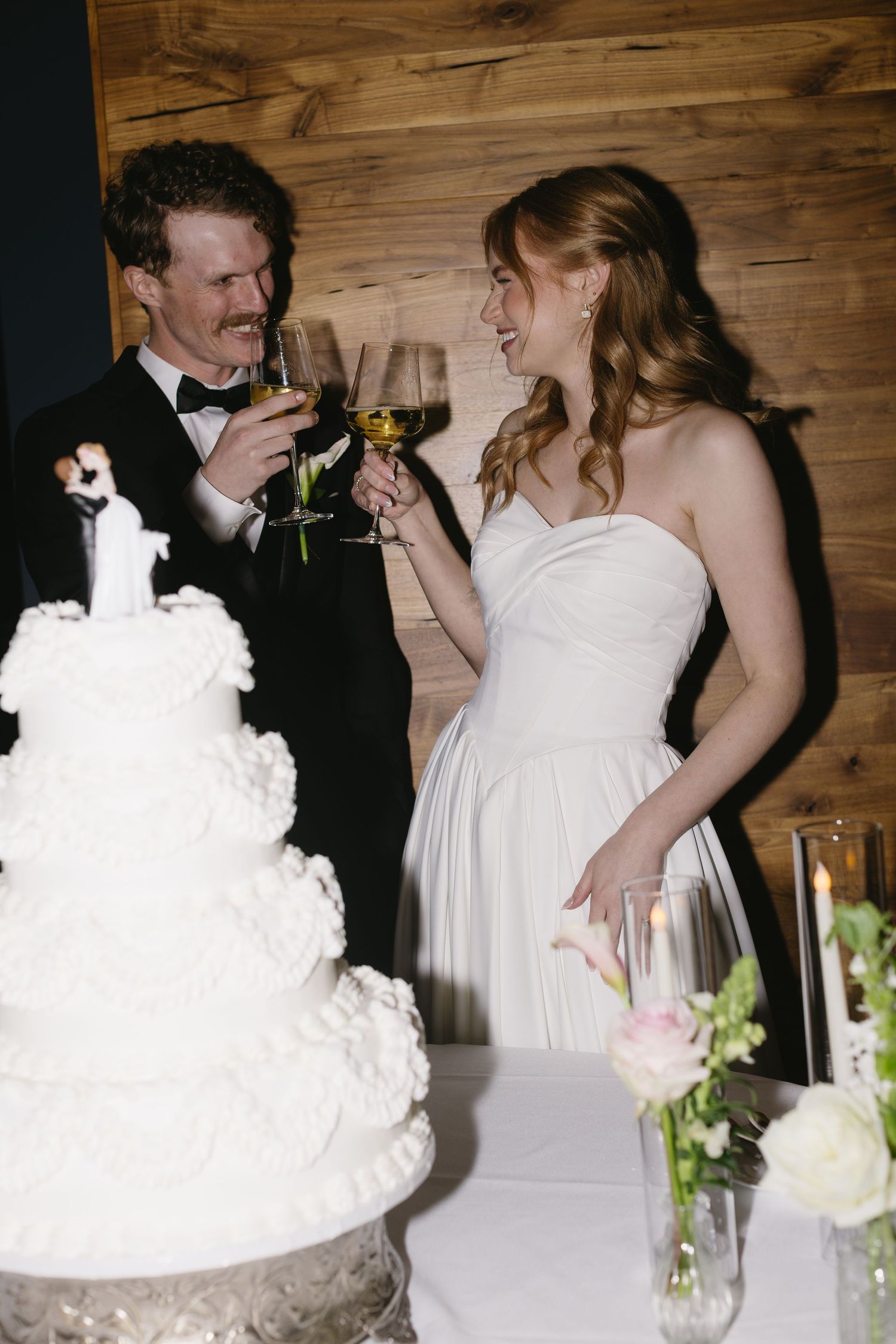 Wedding couple sharing cake and champagne at rustic wooden reception venue.