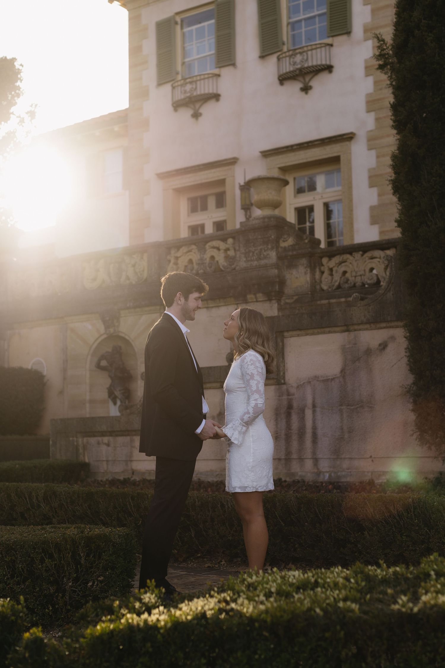 A couple shares an intimate moment at sunset in front of a grand historic building.