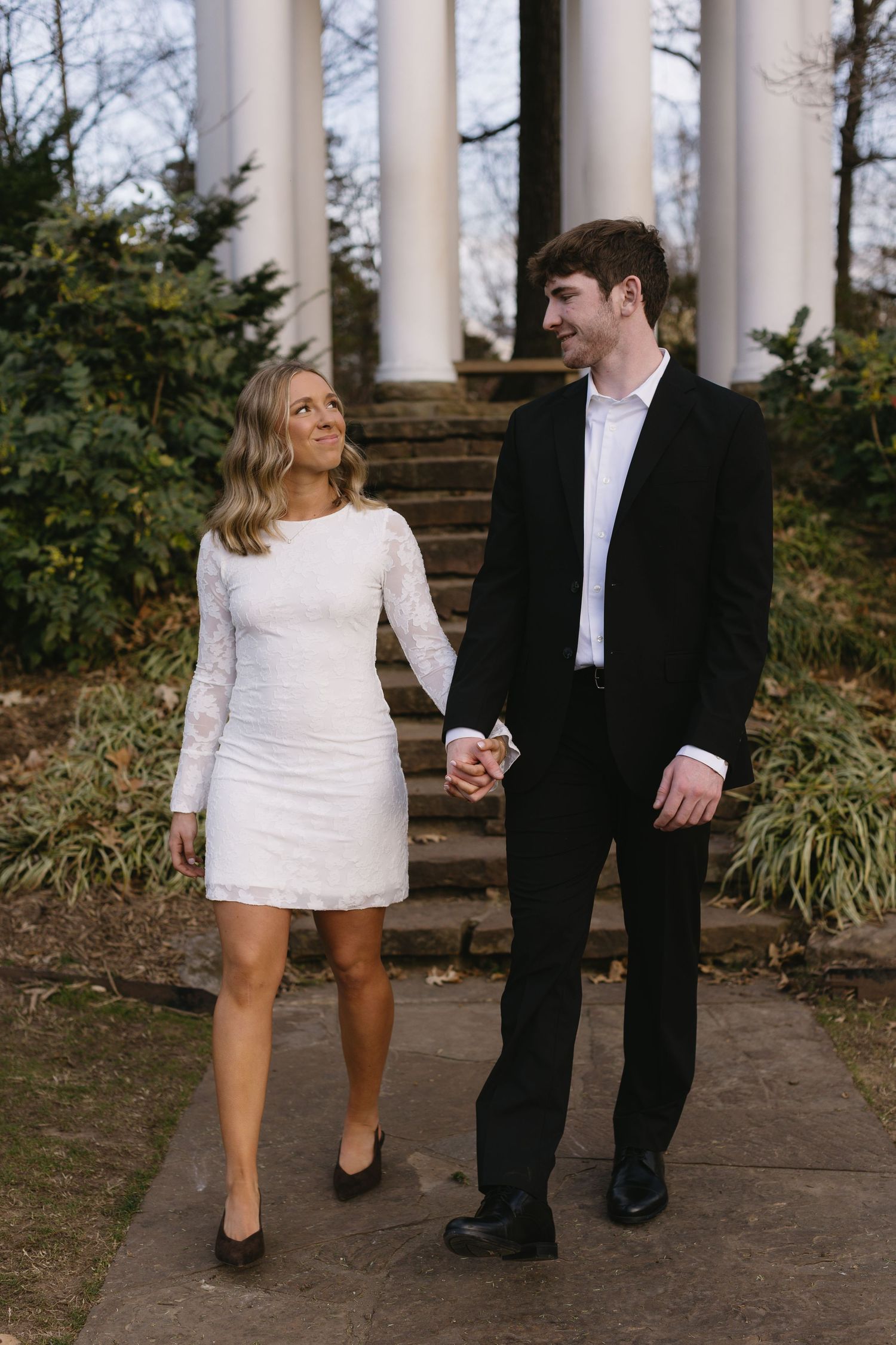 A couple in contrasting black and white outfits walking together among classical columns.