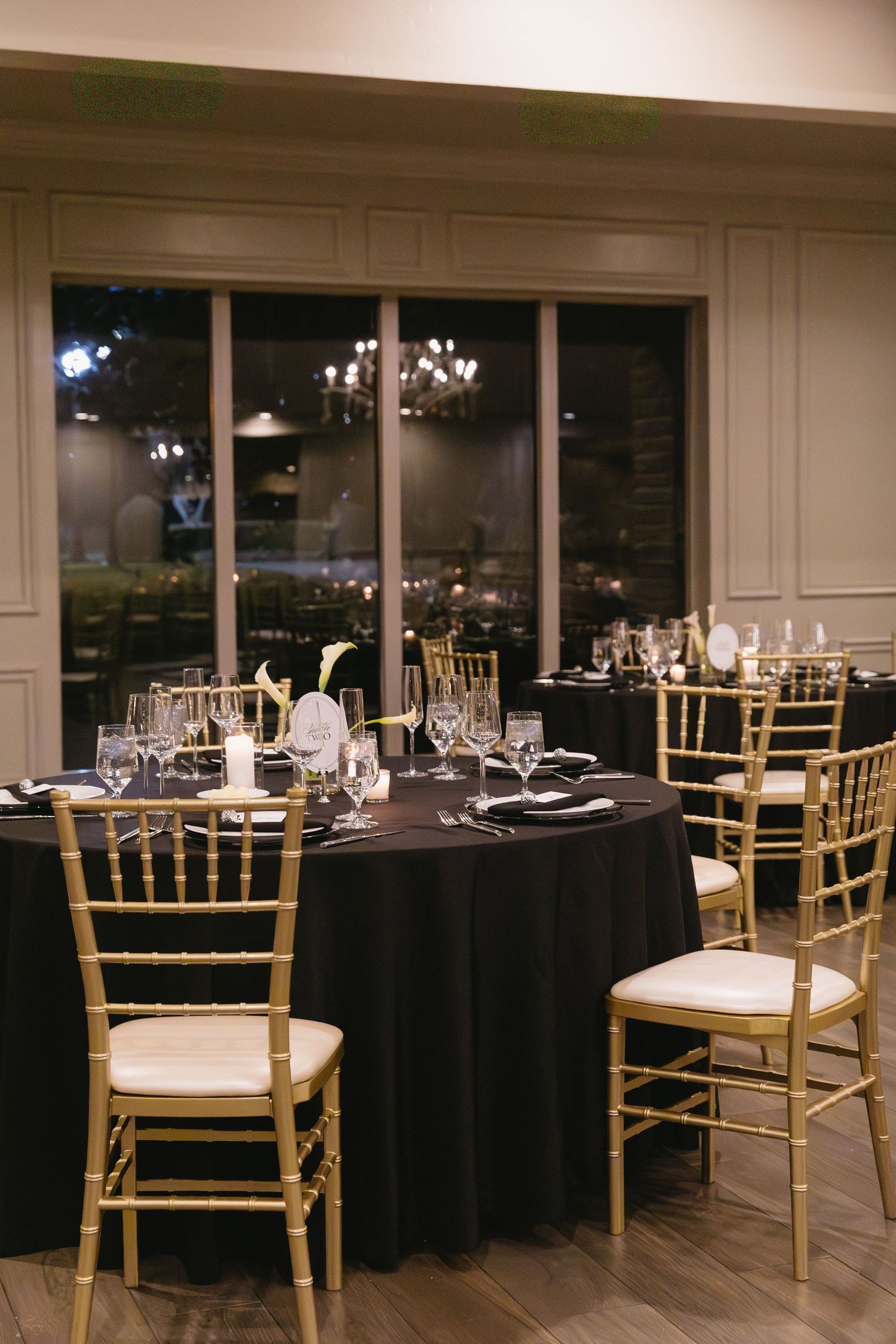 Wedding reception venue with black tablecloths and gold chiavari chairs set for formal dining.