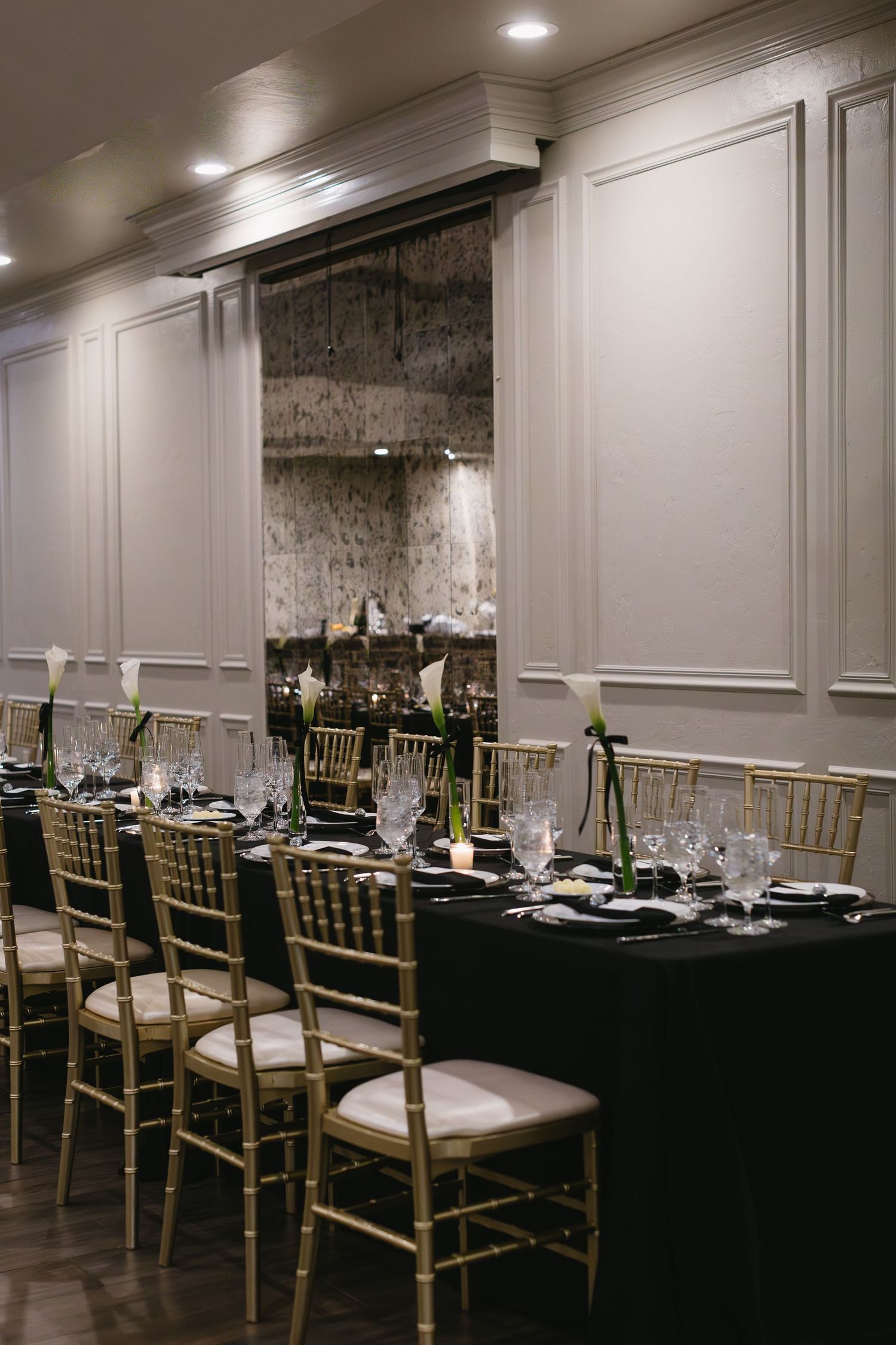 Elegant wedding reception setup with gold chiavari chairs and black tablecloths in a modern venue.