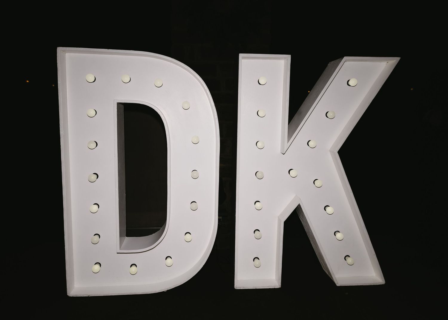 Illuminated marquee letters spelling DK against black background.